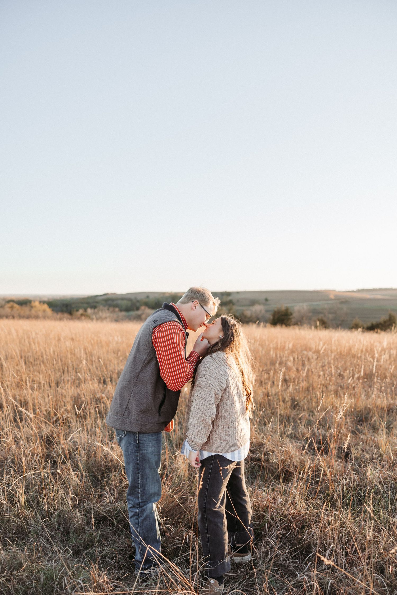 A couple shares a tender moment in a golden field of tall grass at sunset.