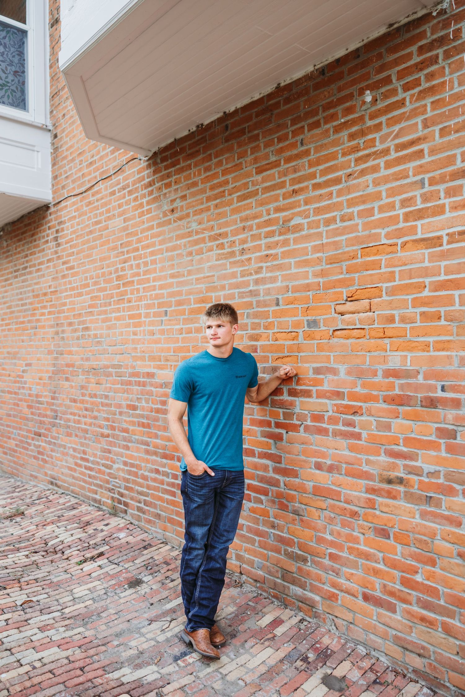 Person in blue shirt leaning against rustic brick wall.