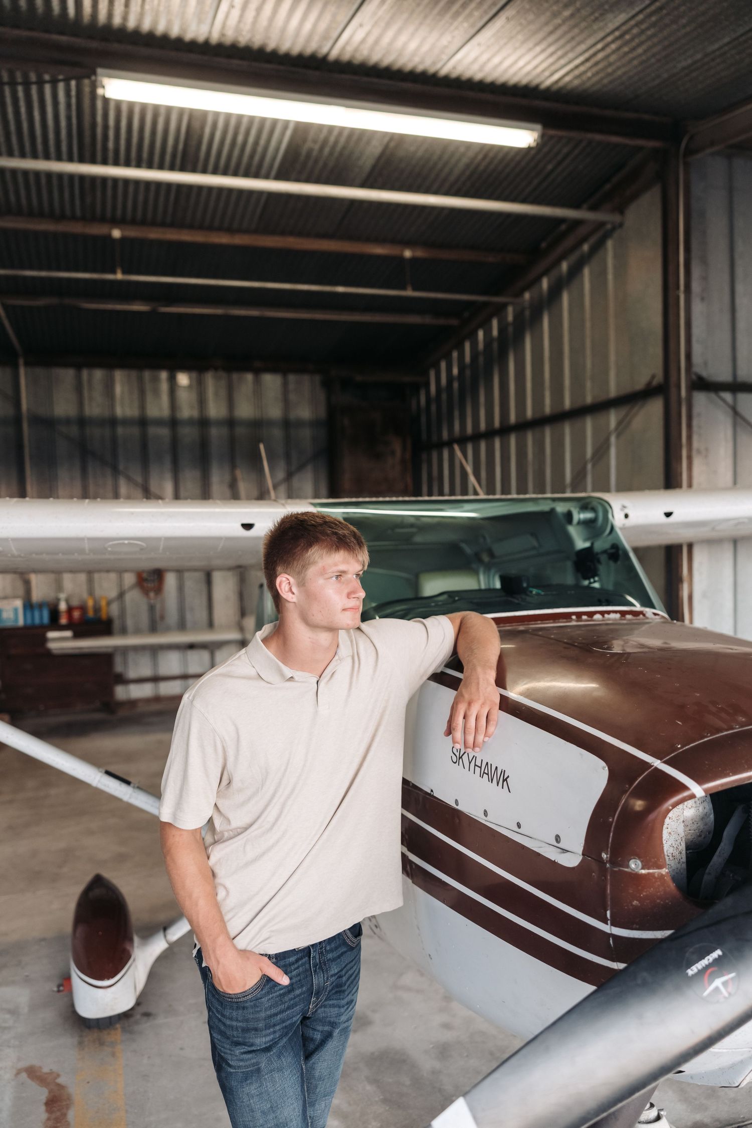 Man in casual attire posing near vintage aircraft in hangar.