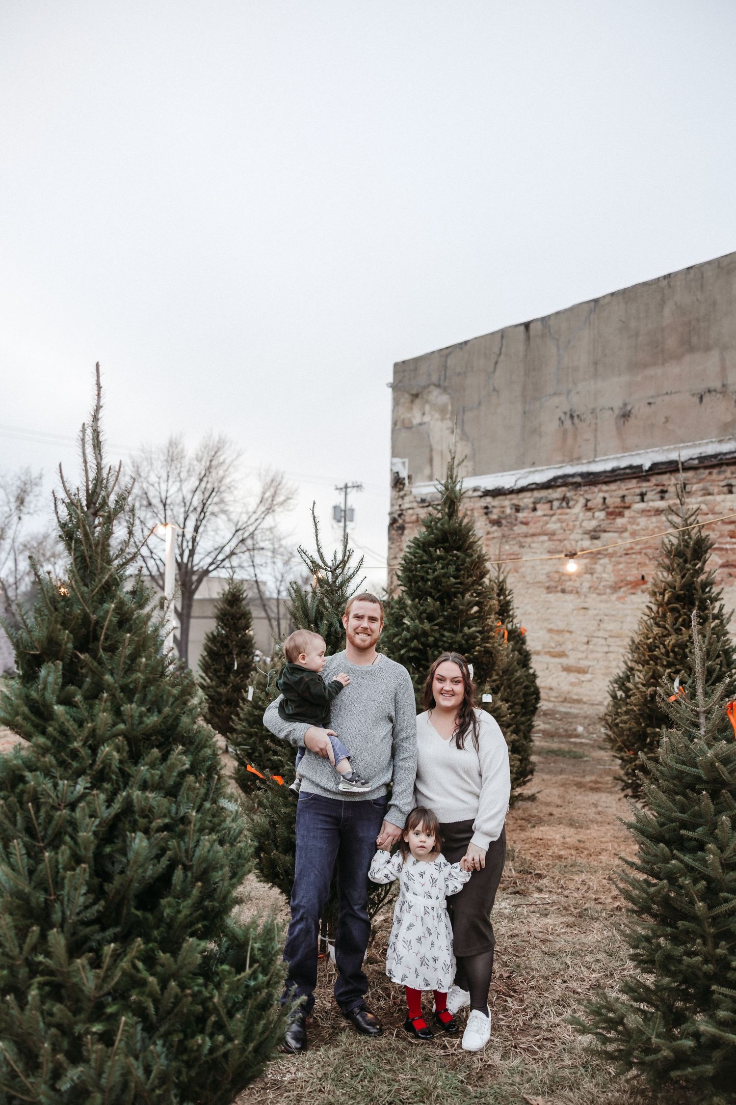Family group poses casually among Christmas trees.