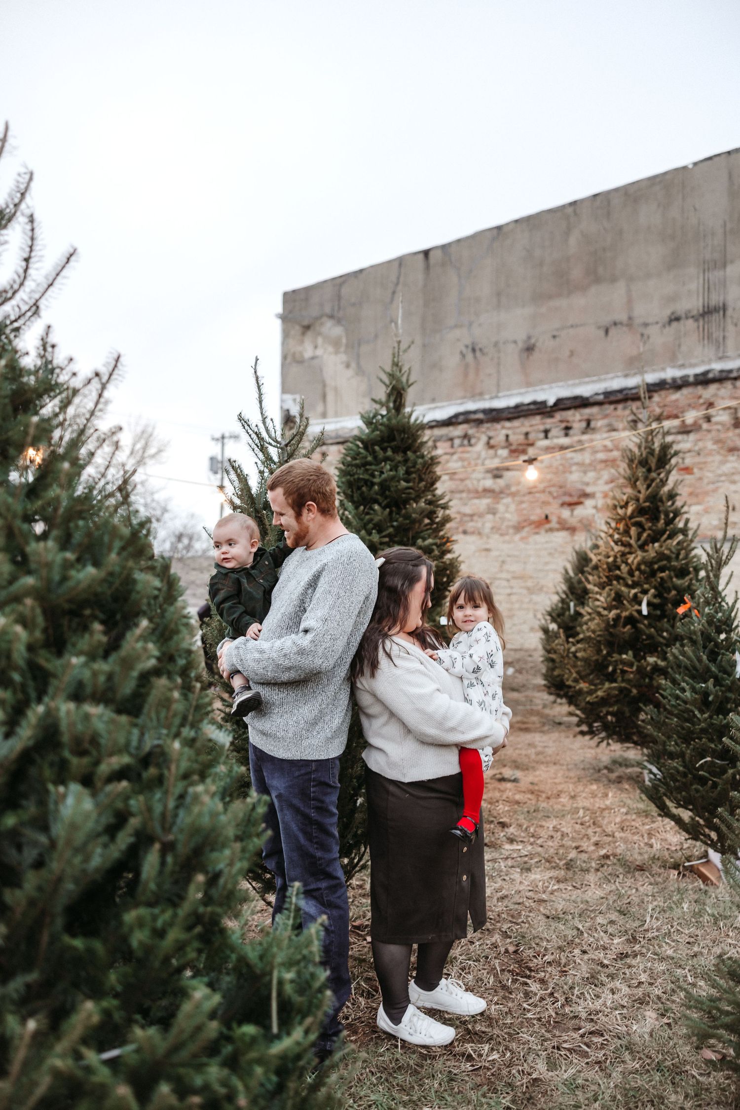Family poses together near evergreen trees.