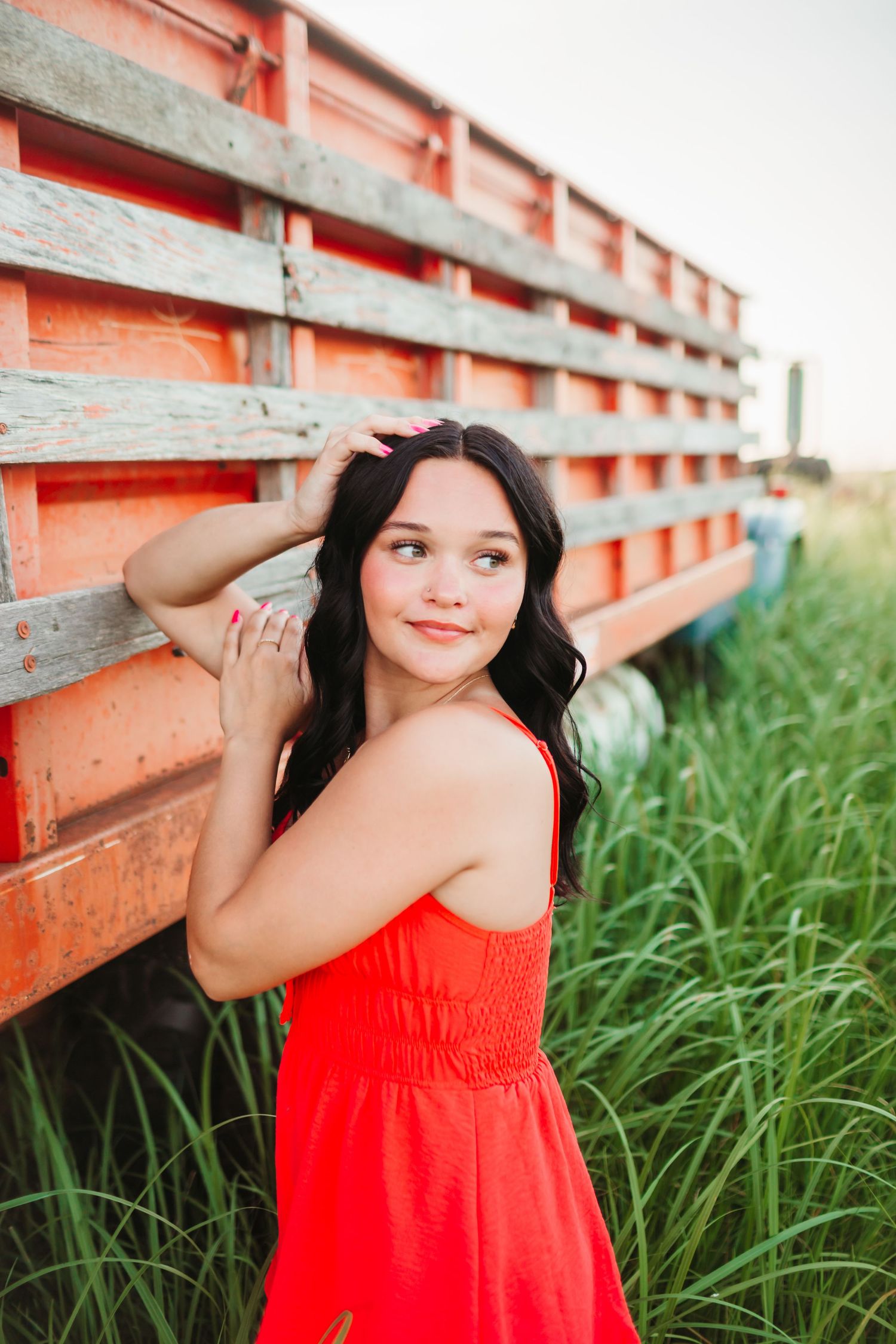 Portrait series against orange vintage truck wearing bright coral dress in tall grass.