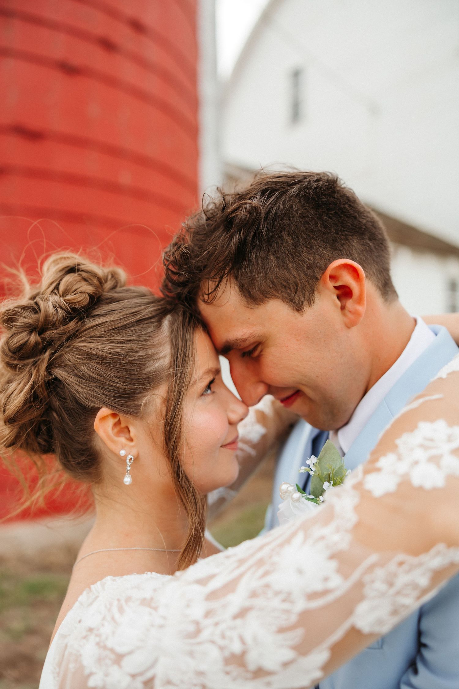 Bride and groom share an intimate moment touching foreheads near a red silo on their wedding day.
