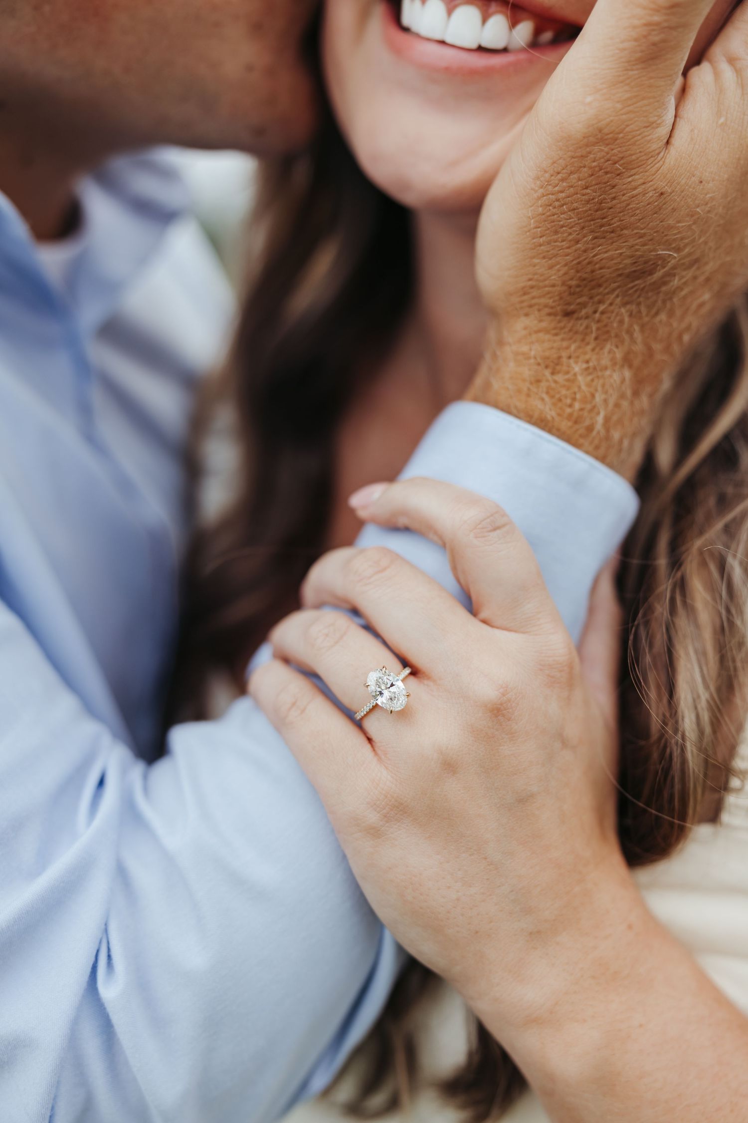 Close-up of hands and a sparkling engagement ring with a bright smile in the background.