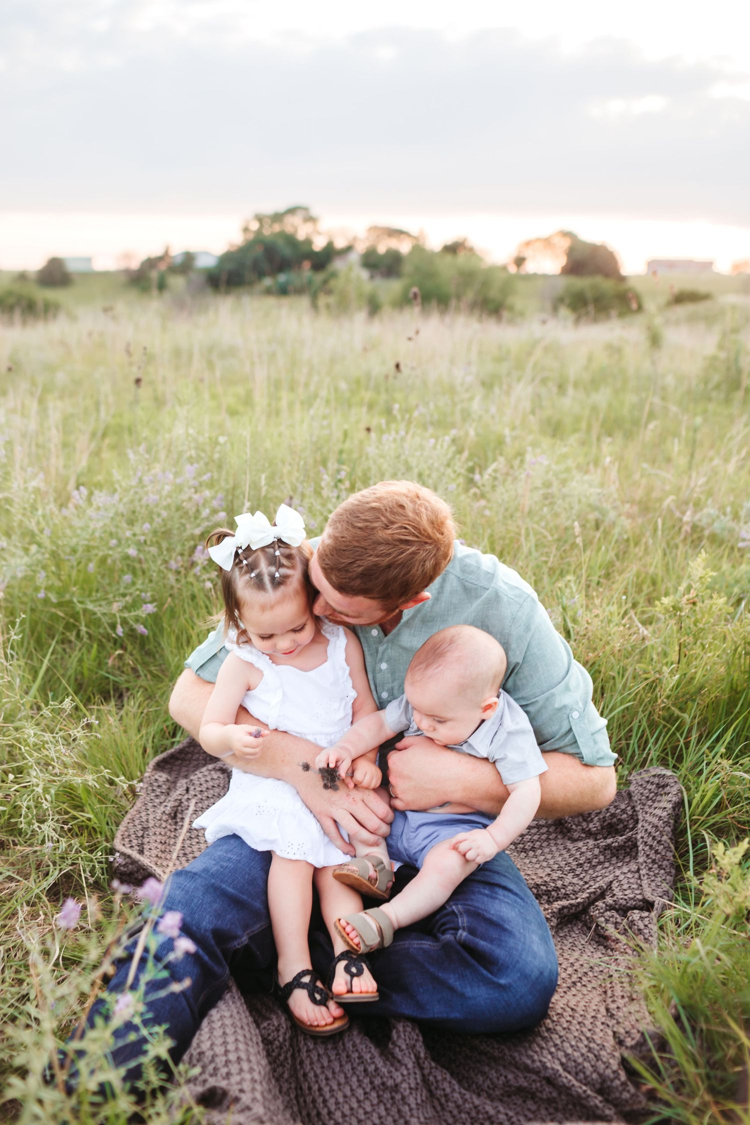 Dad moment captured on blanket in field during sunset.