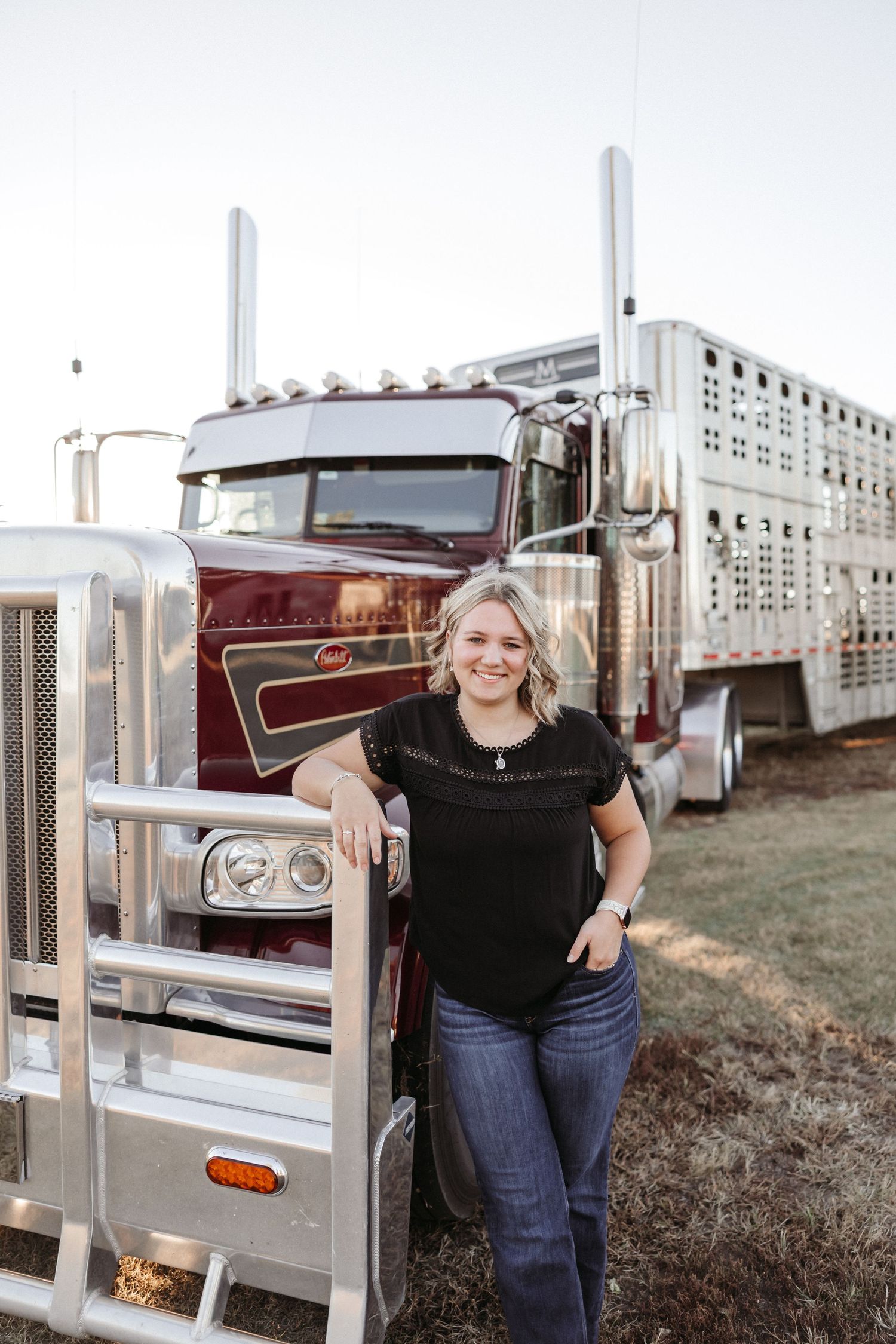 Woman poses near livestock trailers at sunset.