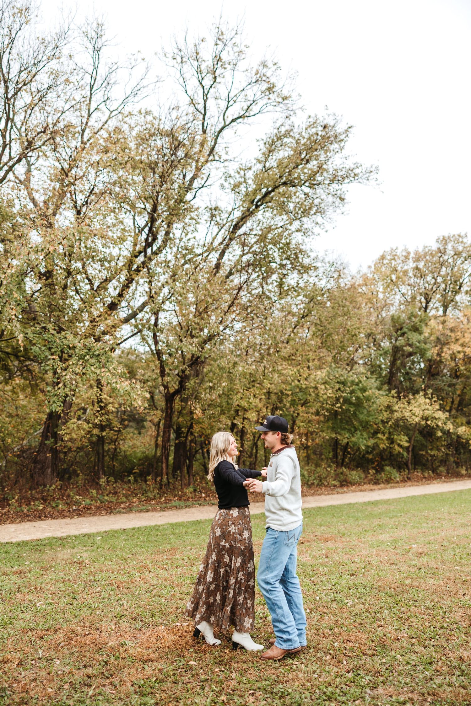 A romantic autumn scene of a couple dancing together on a grassy path surrounded by golden trees.
