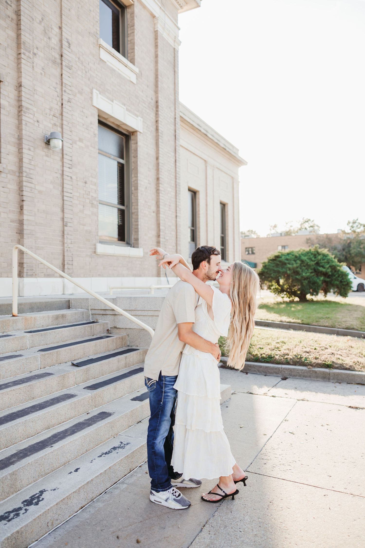 A couple dances and smiles together on the steps of a light-colored building.