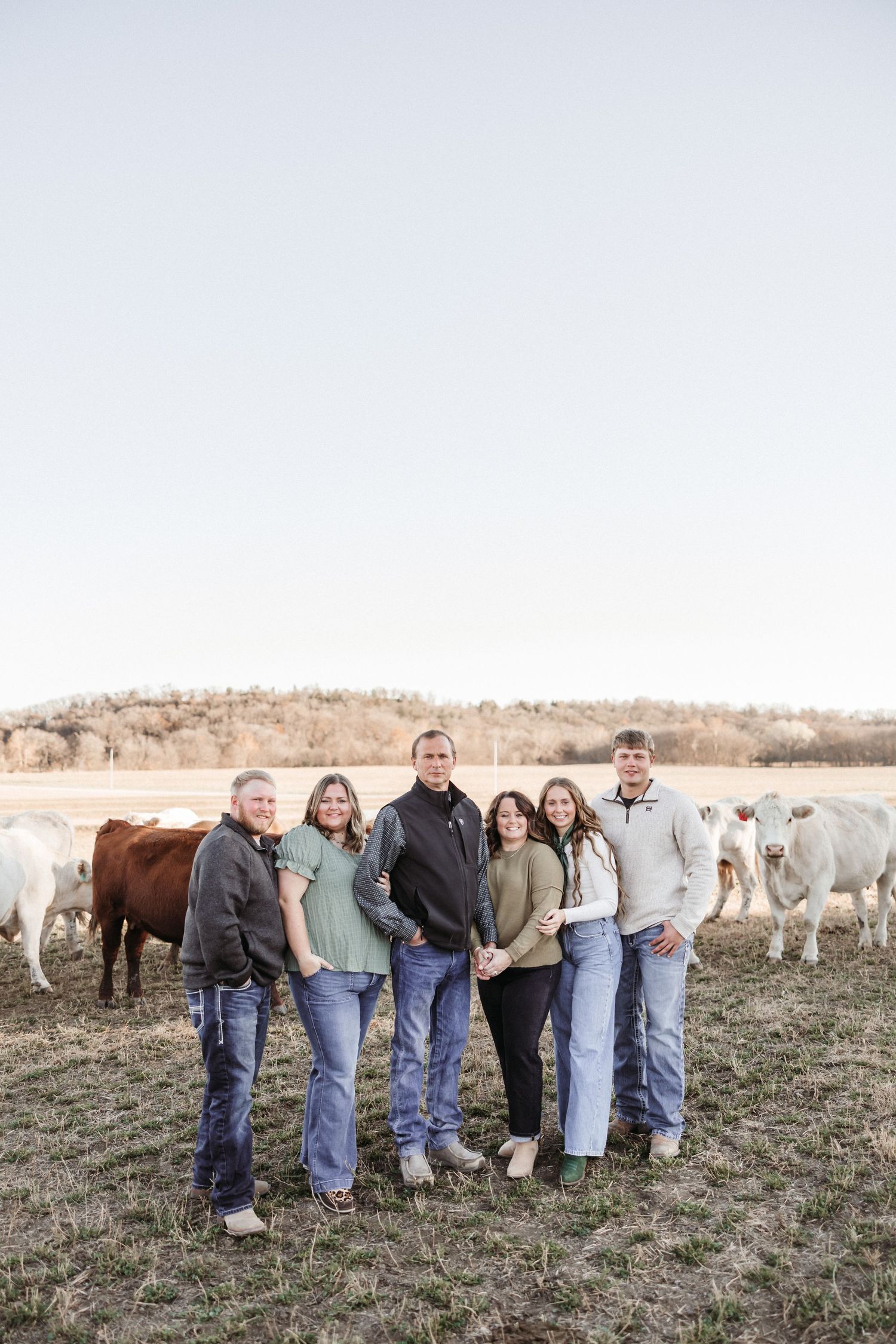 Family members stand together in a line with white and brown cattle grazing in the background.