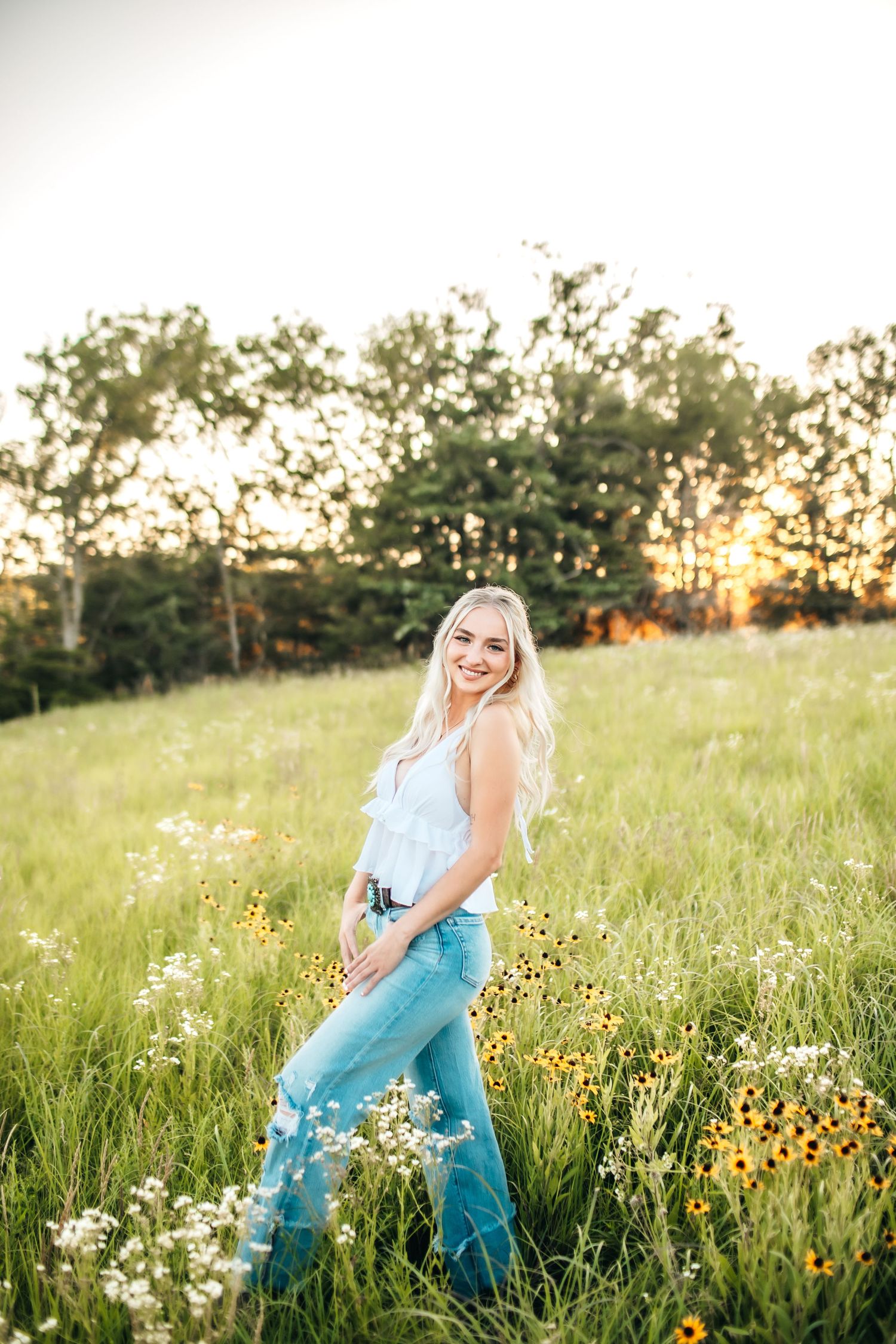 Person in blue jeans and white top walking through wildflower meadow at sunset.