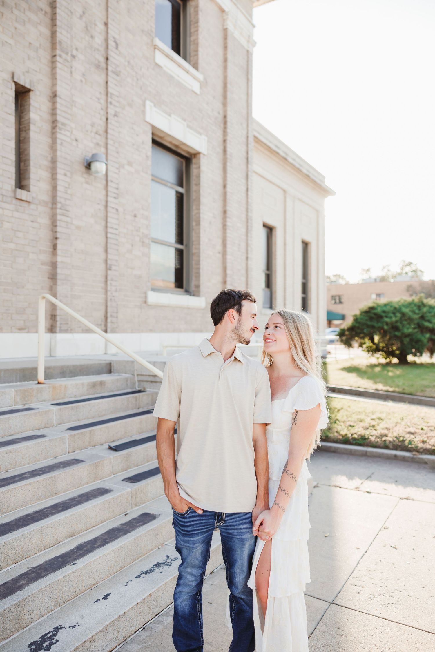 A romantic couple shares a laugh while standing on concrete steps of a historic building.