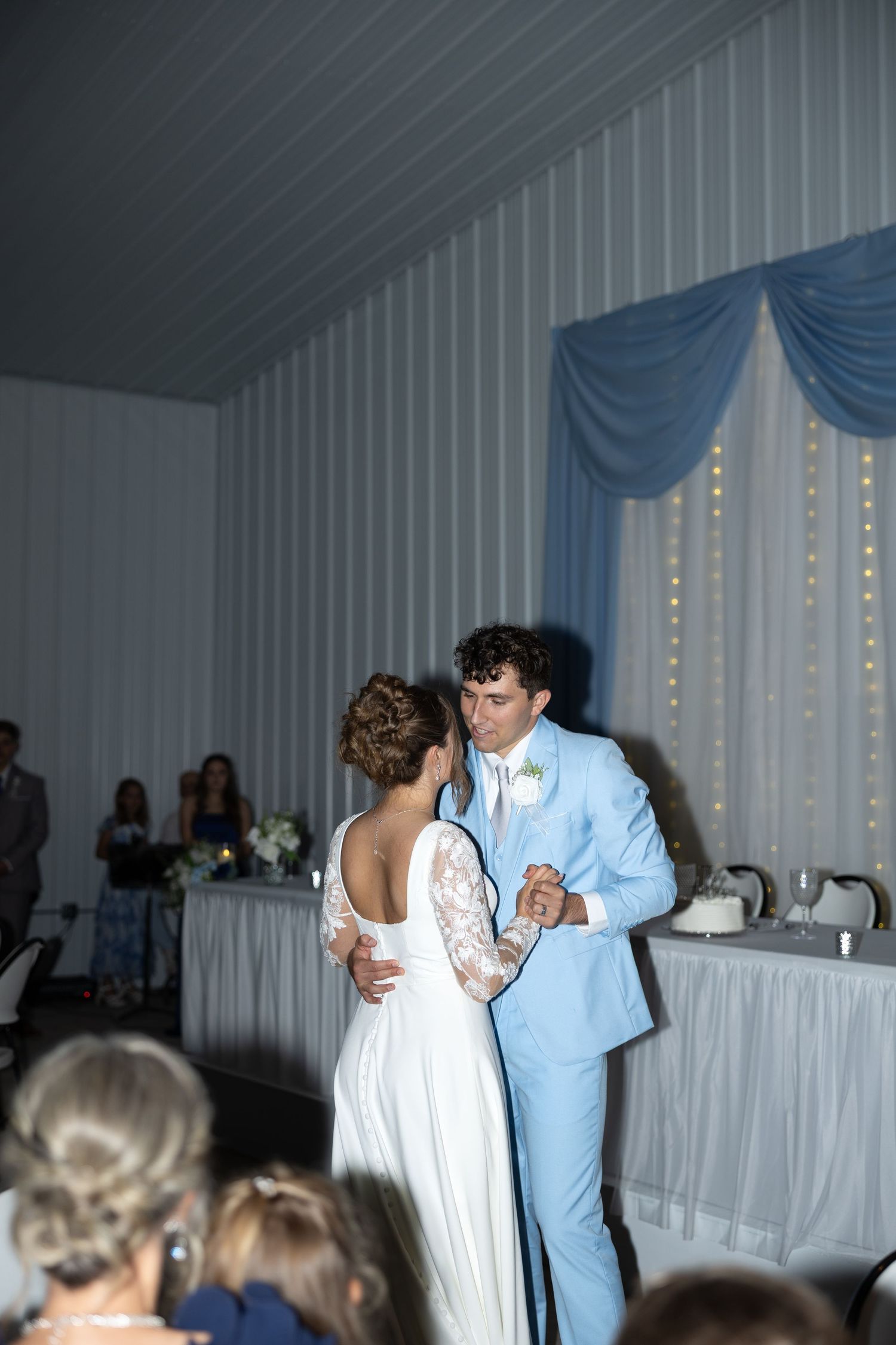 Bride and groom share their first dance at a wedding reception in a white and blue decorated venue.