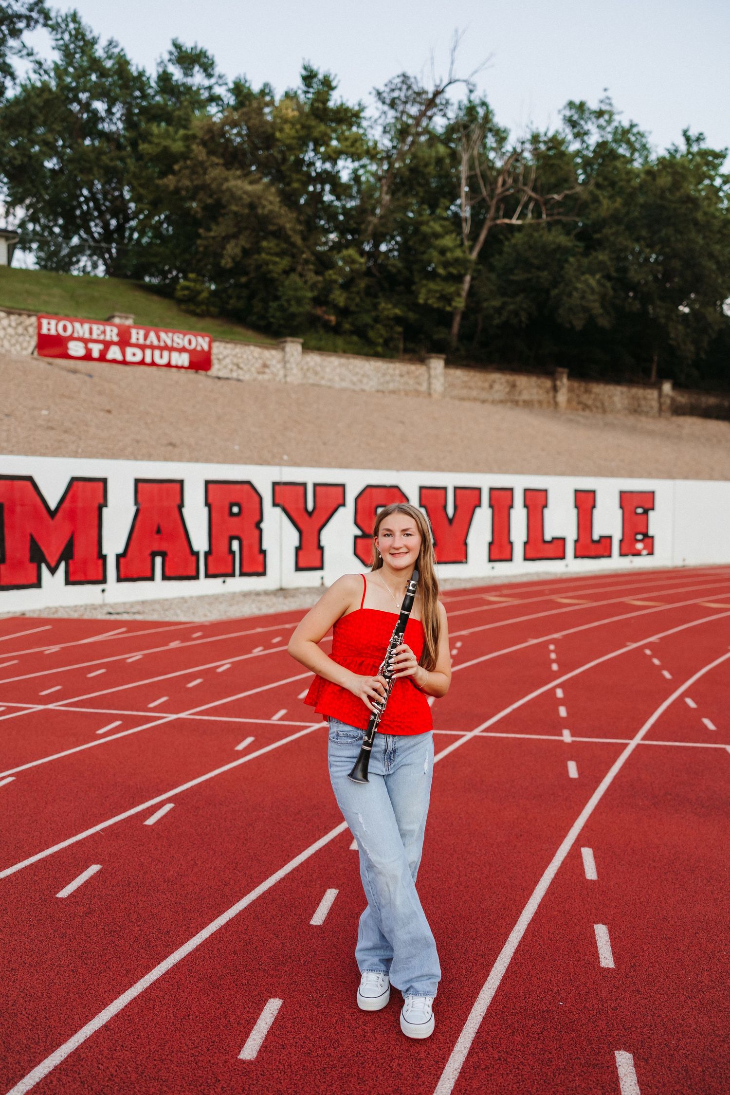 Young woman holding a clarinet on Marysville track at Homer Hanson Stadium, wearing red top and jeans.