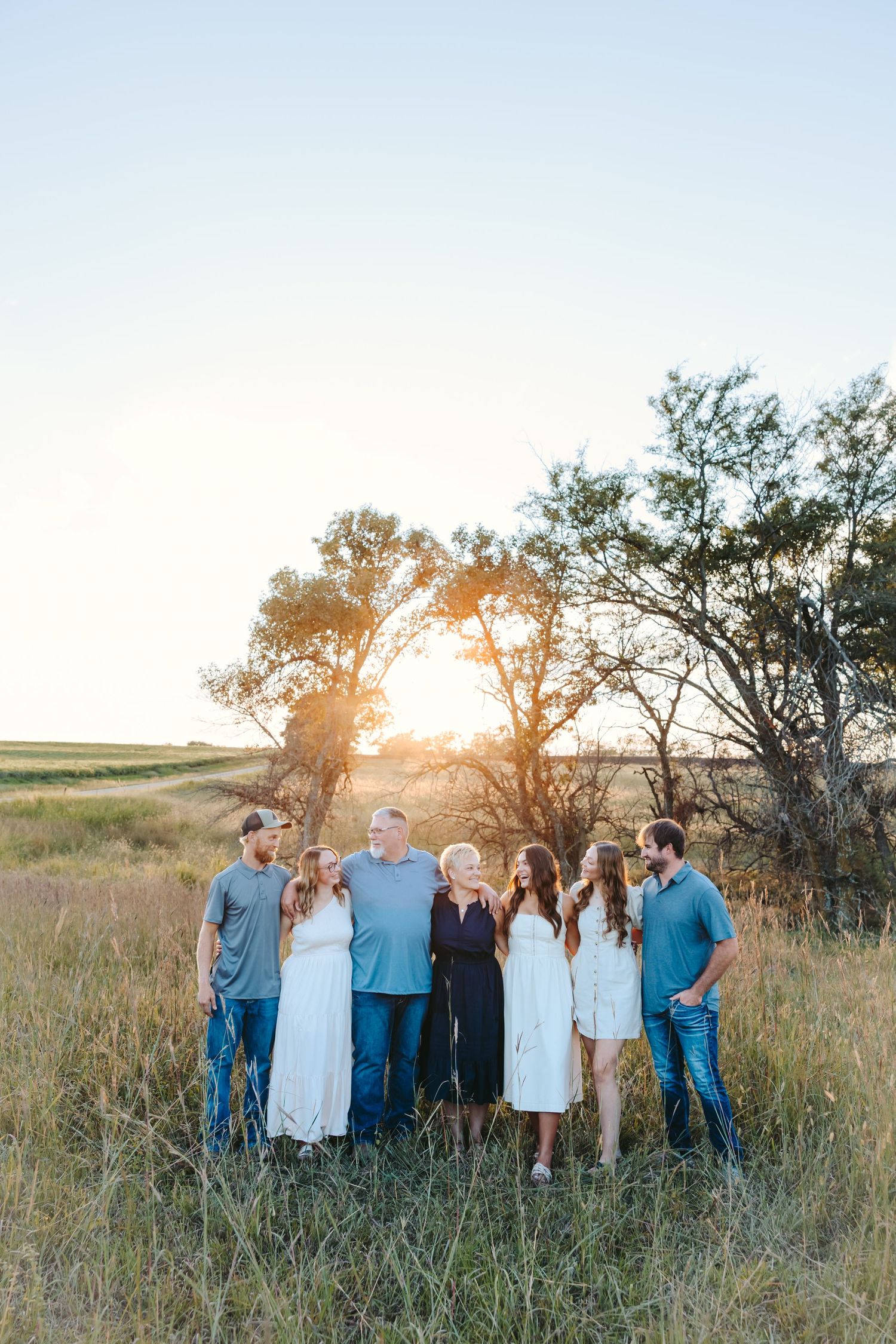 Family group poses casually in a line across a scenic field during golden hour.