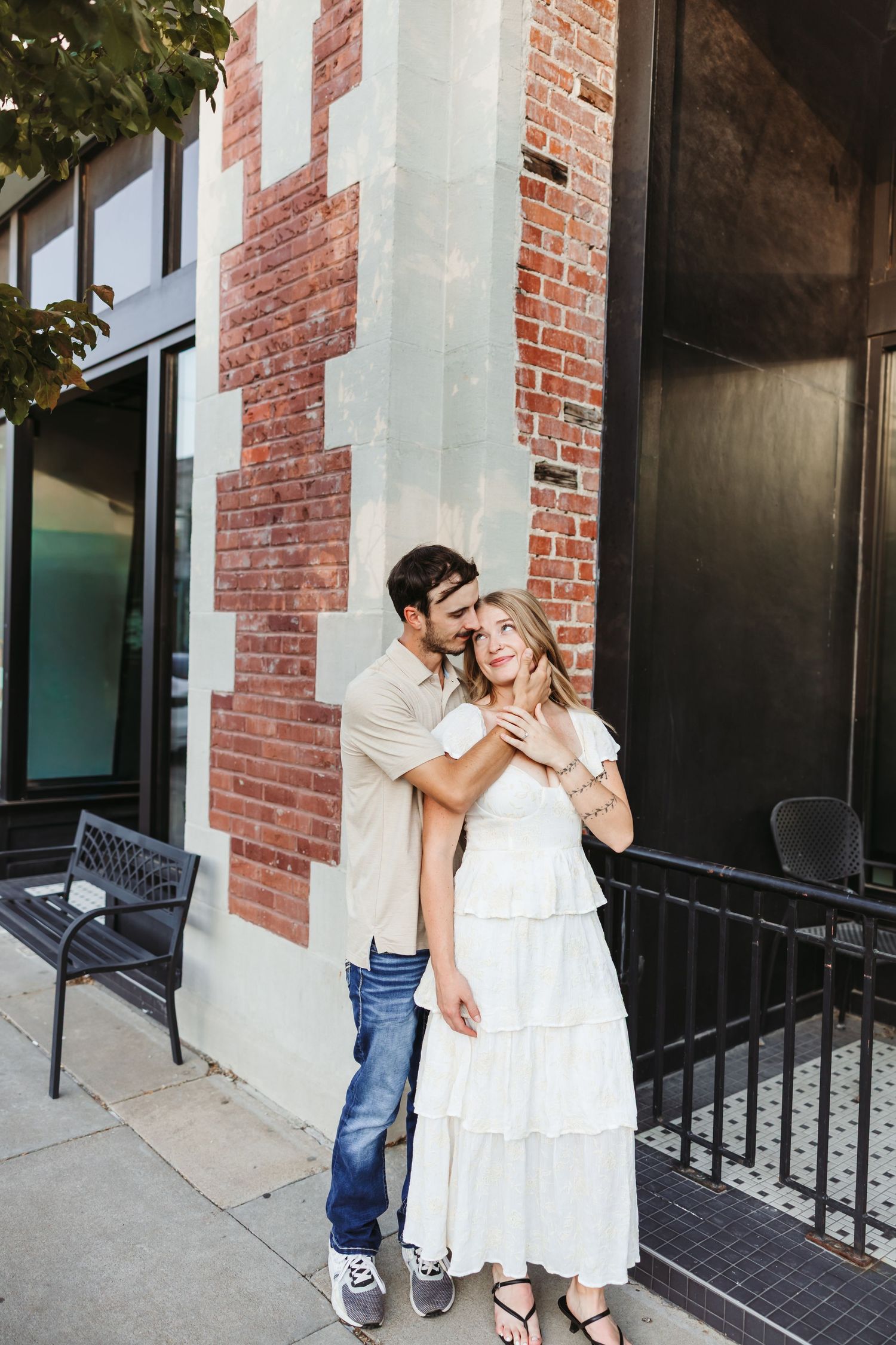 A couple shares an intimate moment against a rustic brick wall exterior.