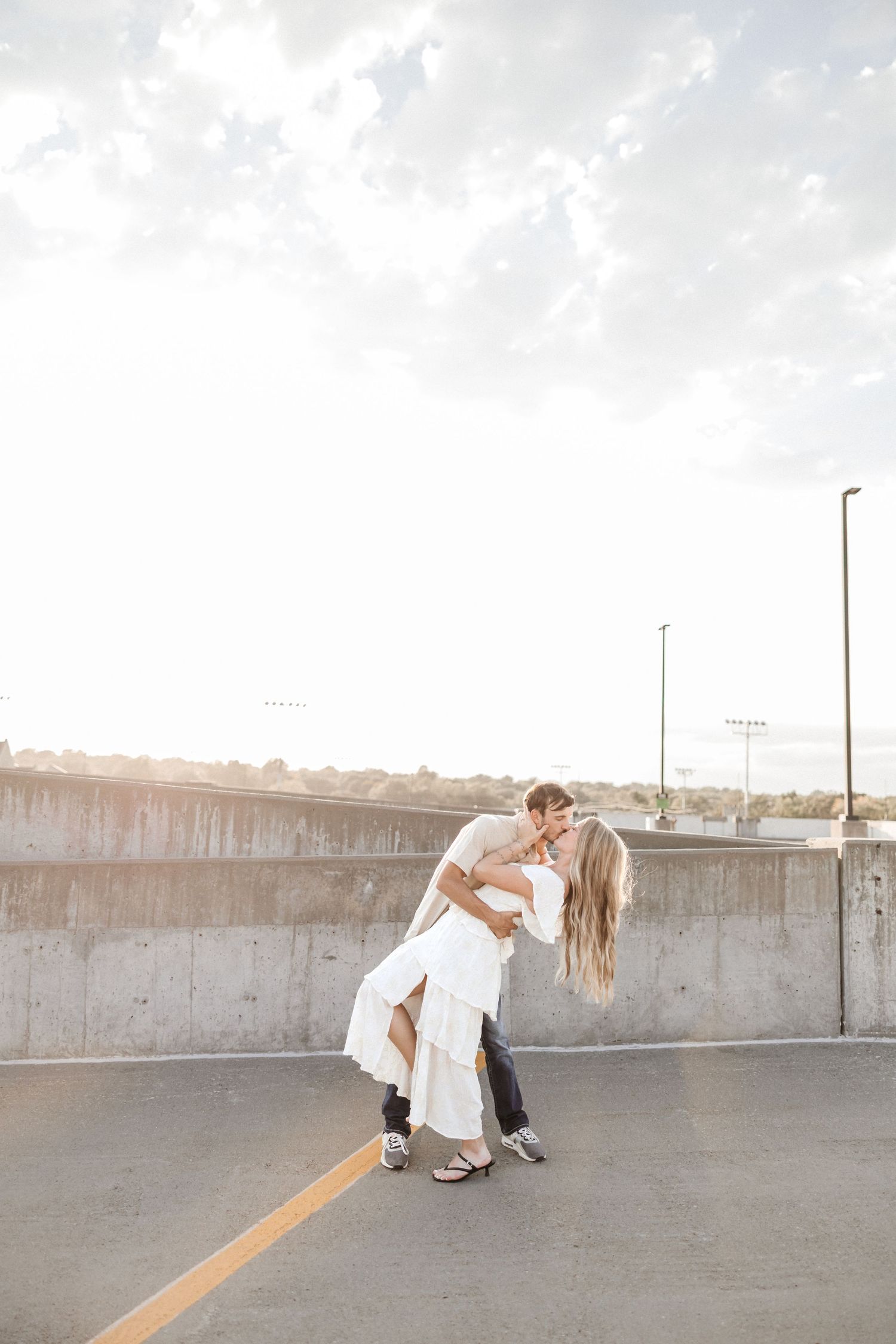 A couple shares a romantic dip pose on a parking structure at sunset.