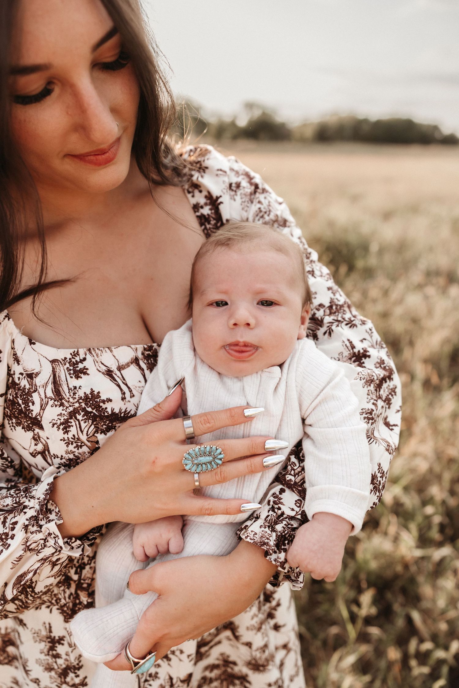 A tender moment between mother and baby in a sunlit field, wearing floral and white outfits.