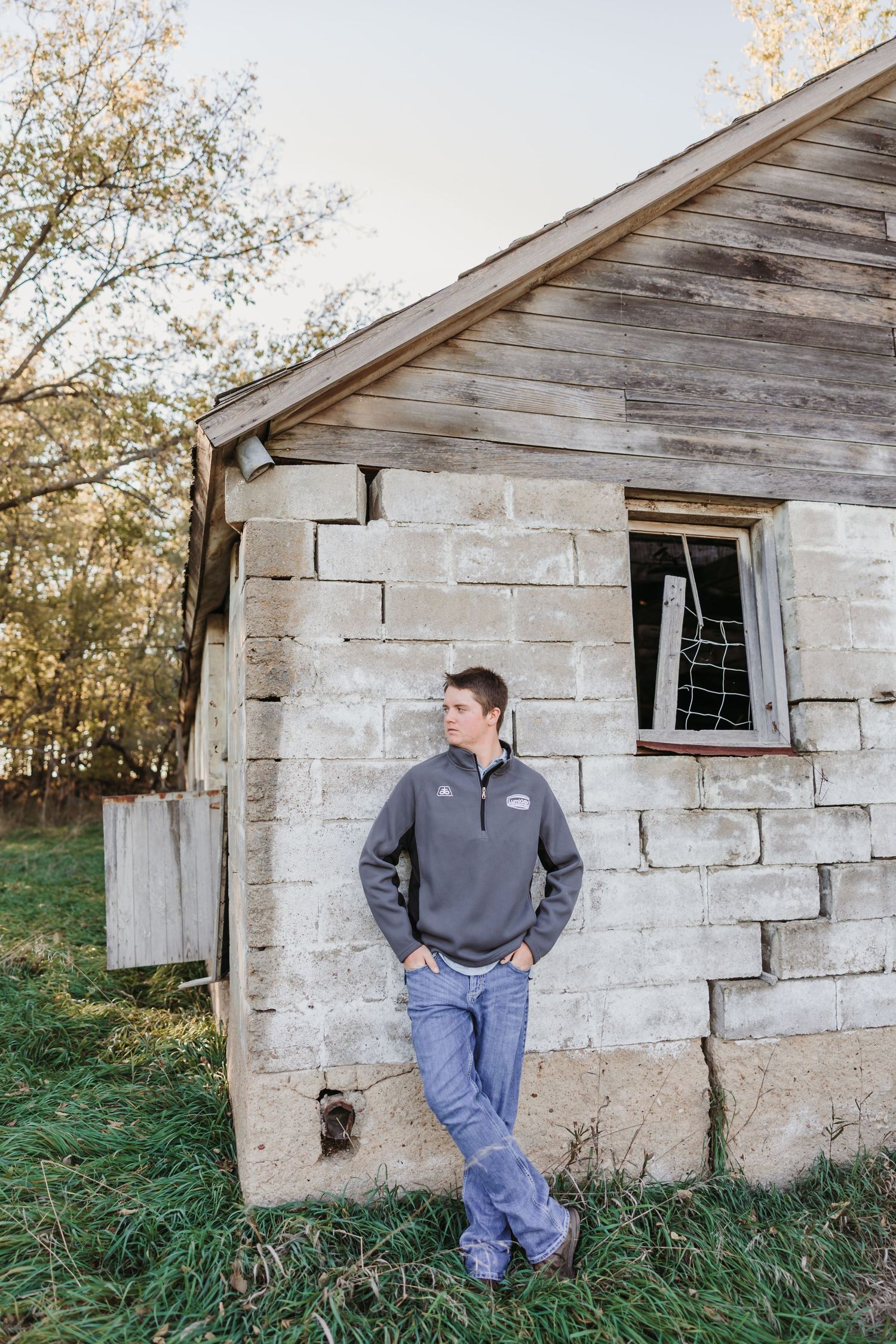 Man in gray sweatshirt leans against weathered stone building wall.