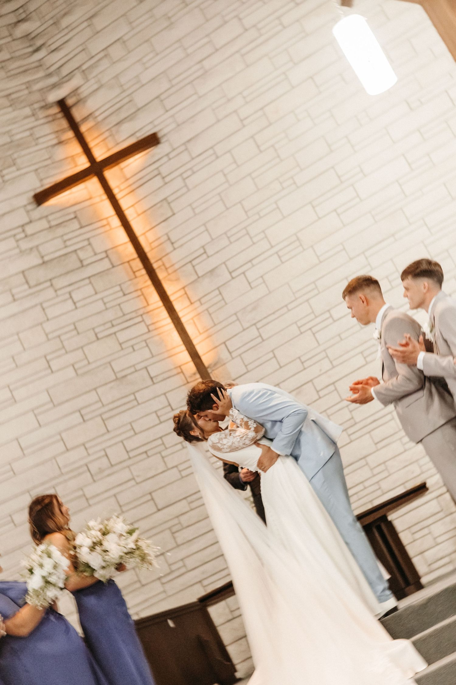 Bride and groom share a romantic dip kiss at the altar in a church wedding ceremony with bridesmaids and groomsmen.