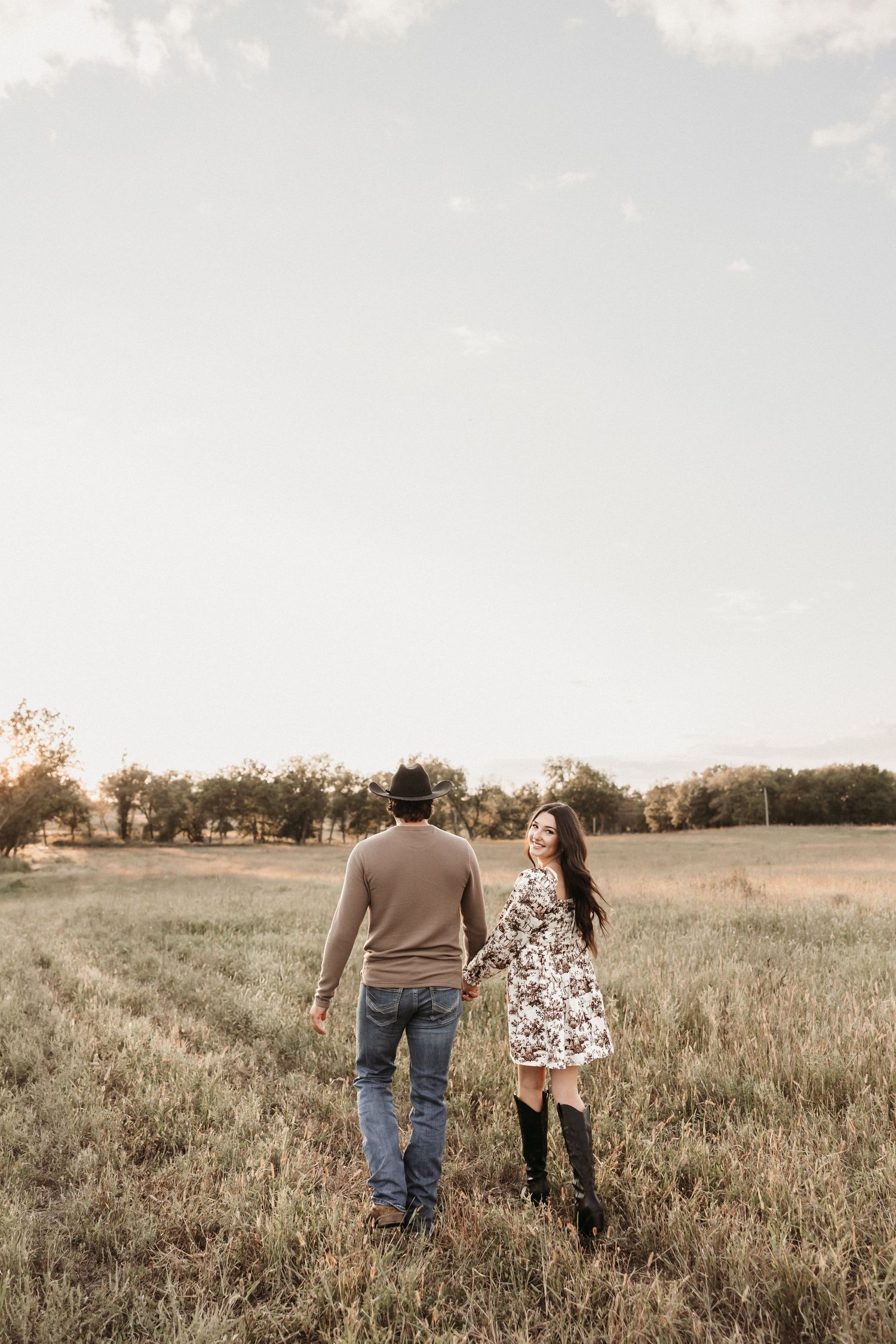 A couple strolling together through a rustic field during golden hour.