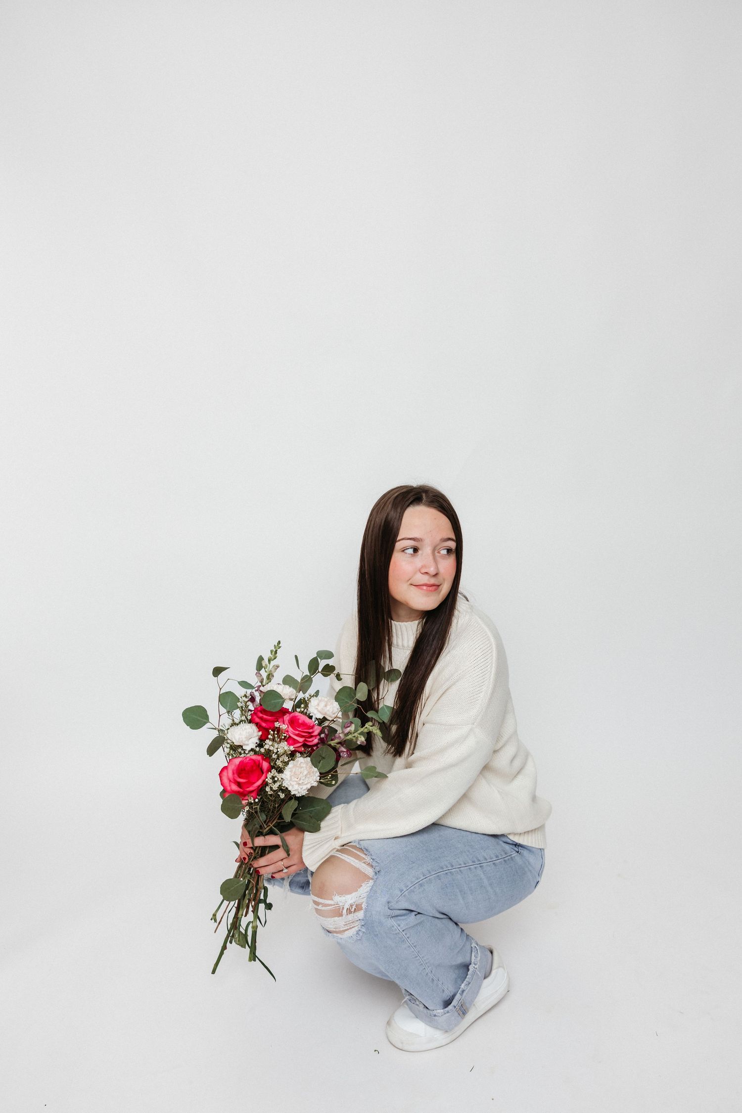 Kneeling with beautiful a flower bouquet against white backdrop.