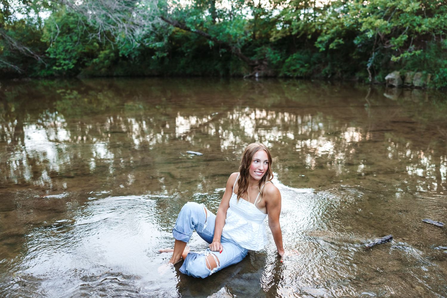 Woman in casual wear splashes playfully in shallow creek water.
