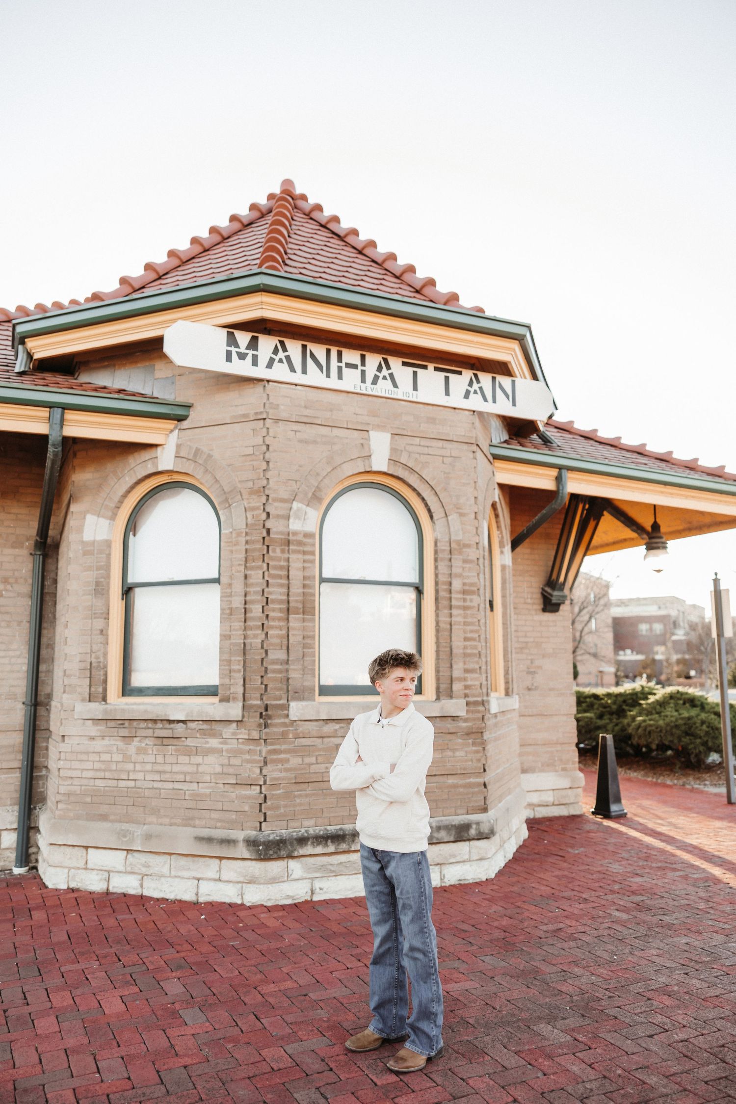 Boy standing in front of Manhattan train station building with brick architecture and red tile roof.