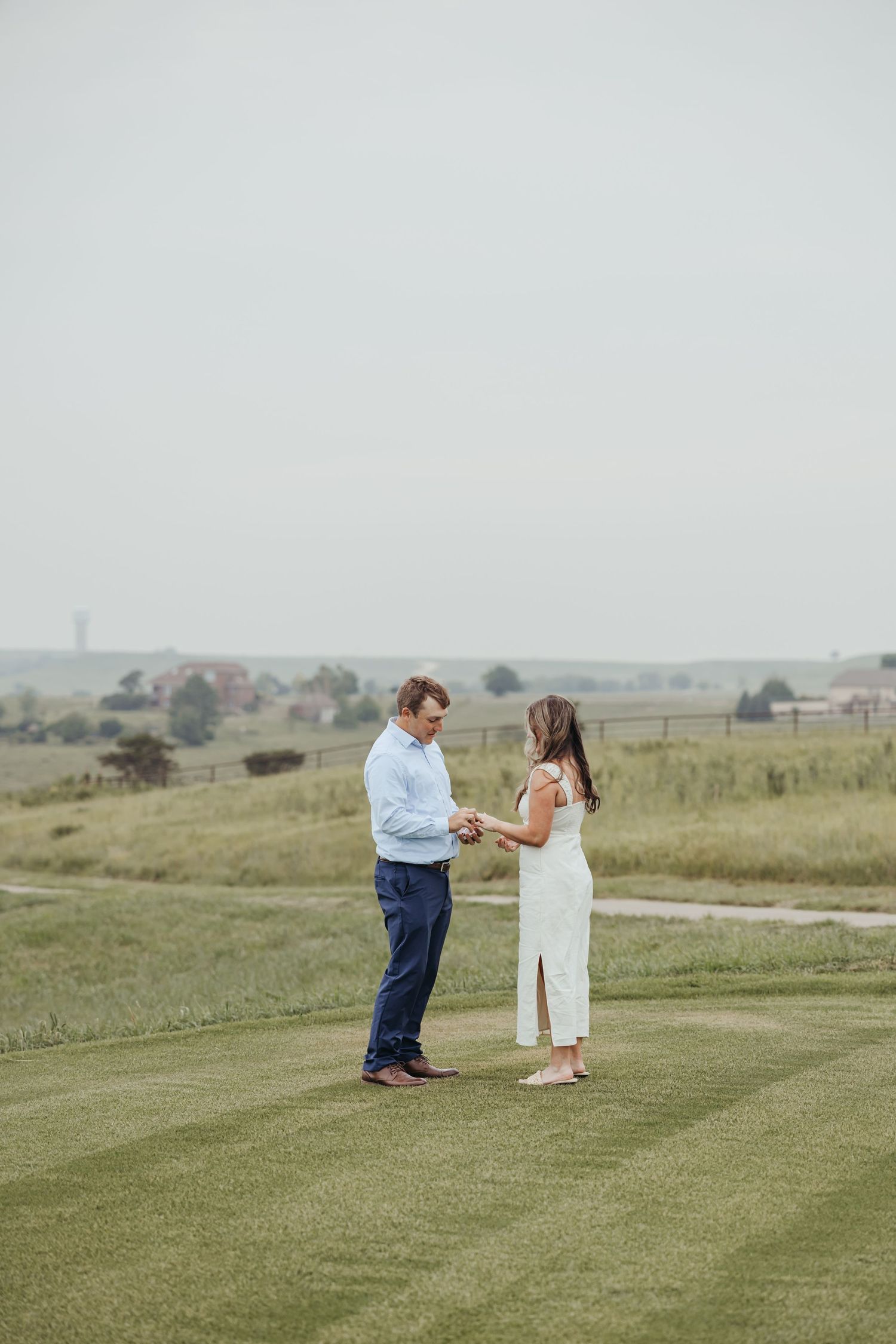 Two people stand close together on a lush green golf course surrounded by rural landscape.