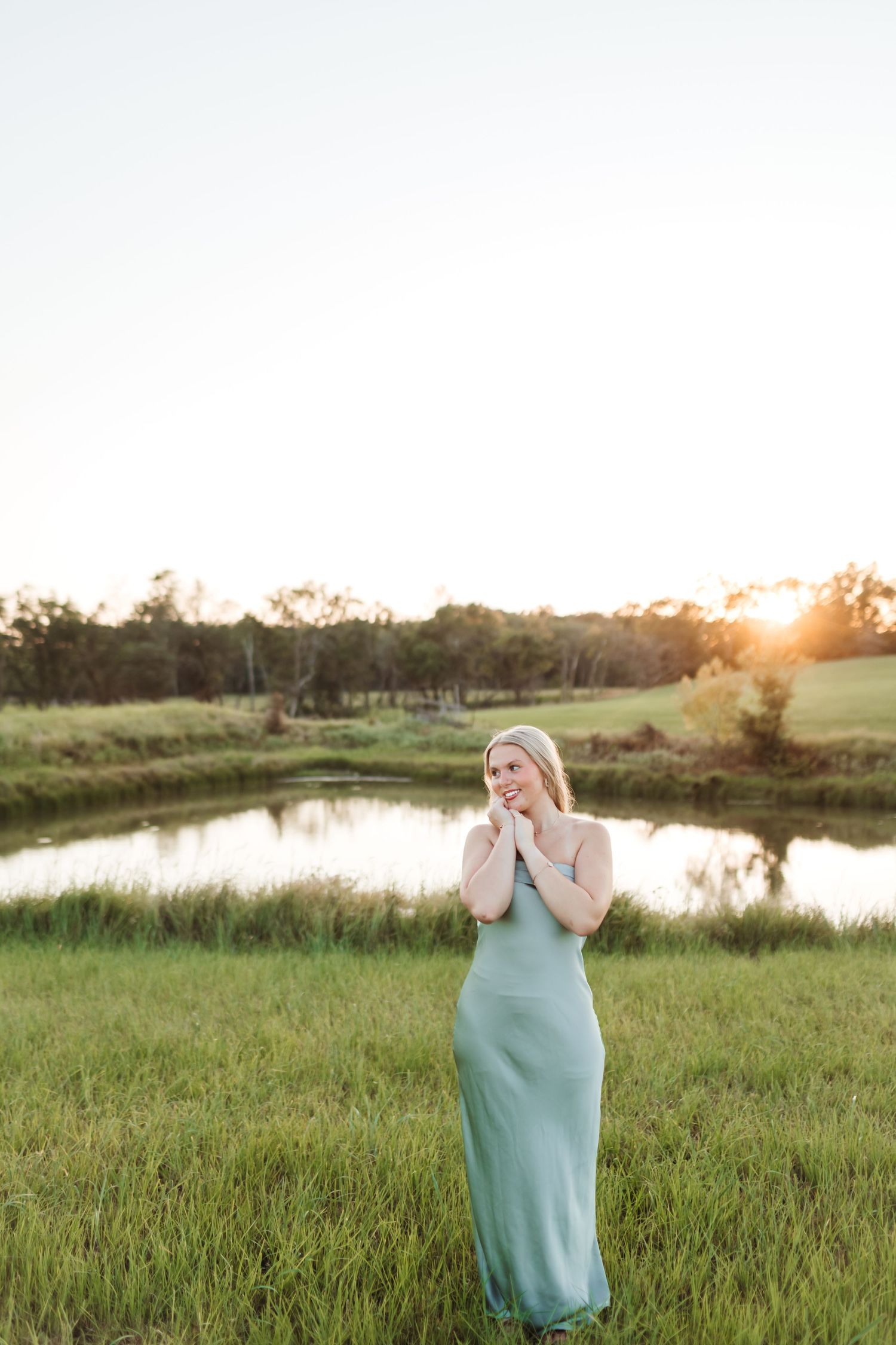 Ethereal portrait in mint green dress against sunset pond landscape.