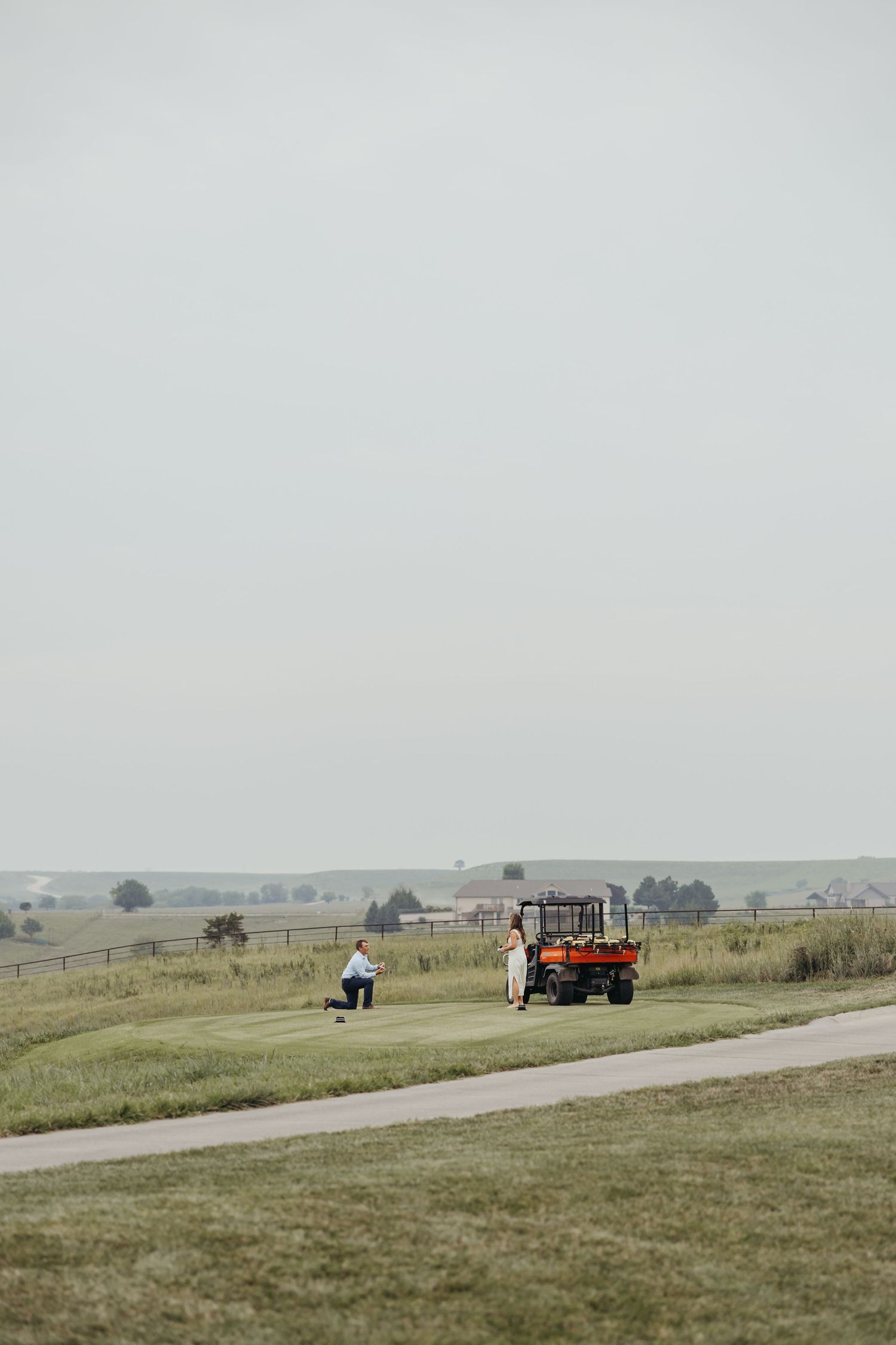 An engagement happening with a distant view of a golf cart and couple on a scenic course with rolling hills.