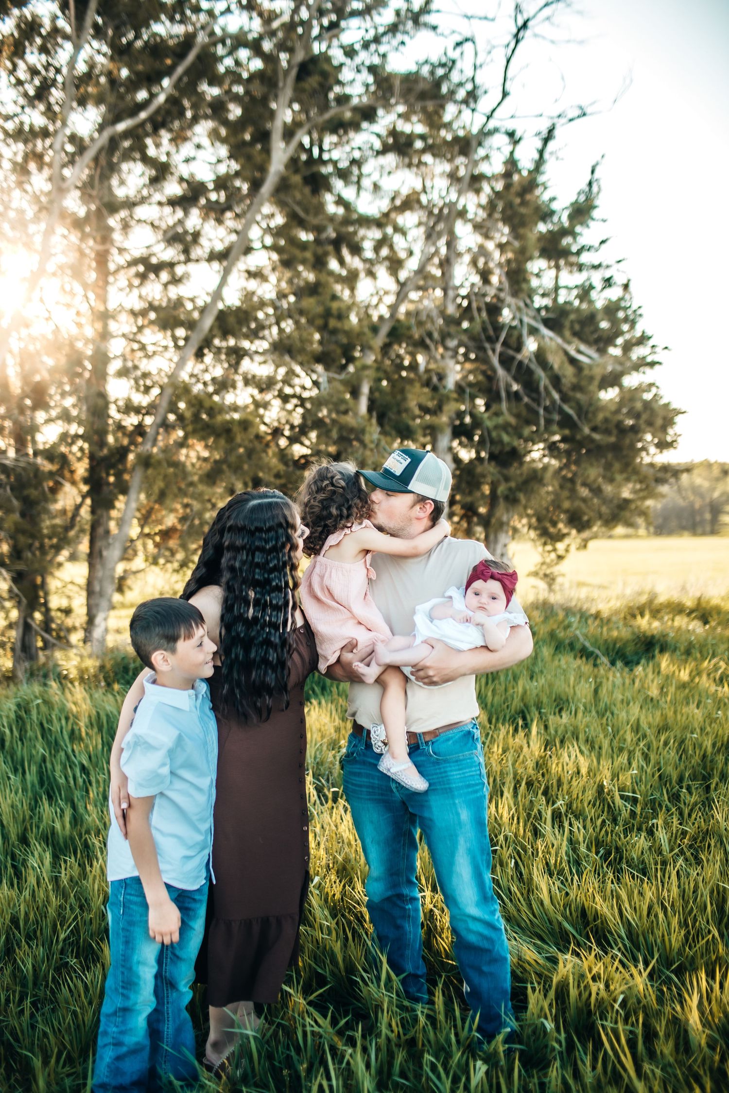 Family cuddled together in tall grass field during golden hour.