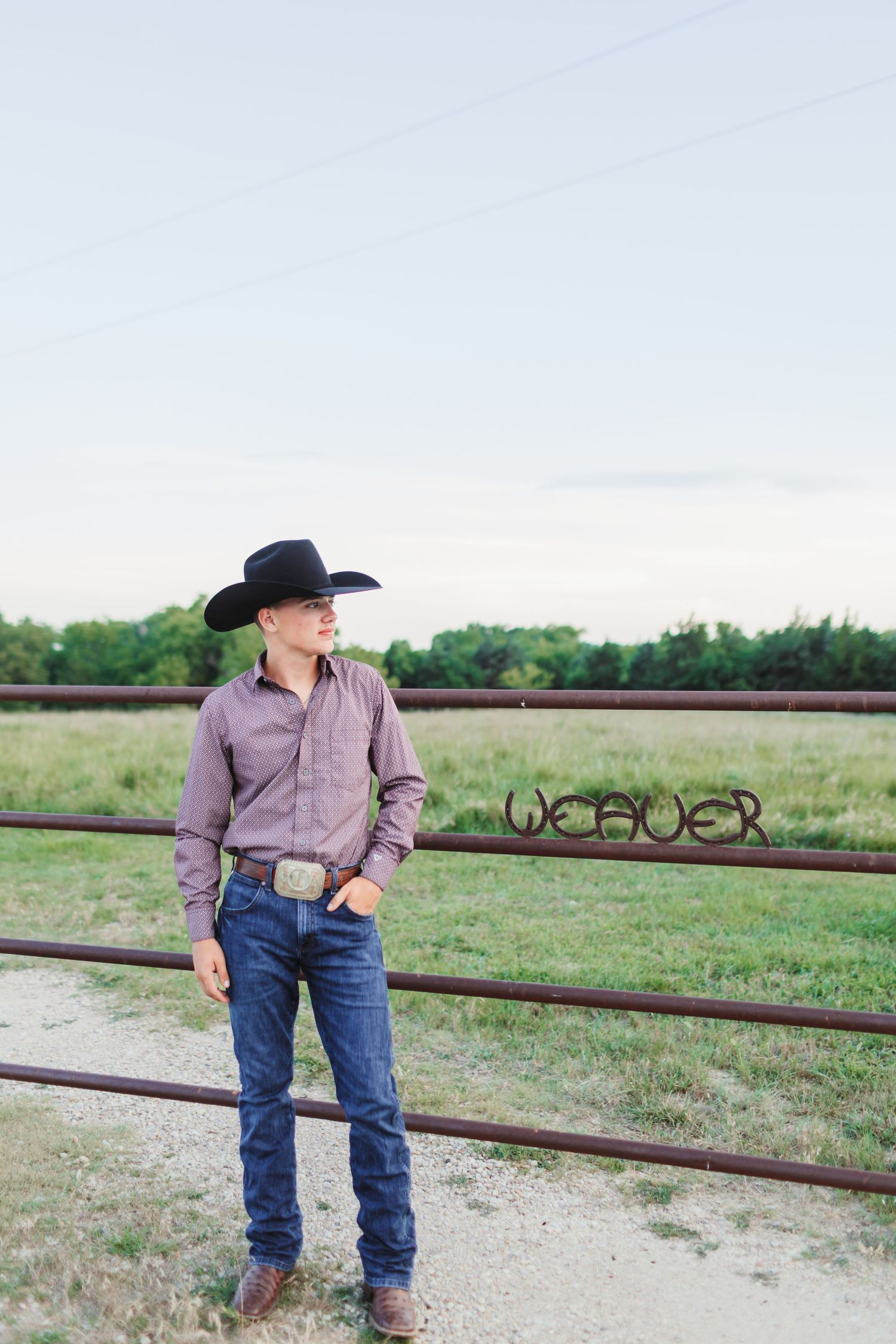 Western style portrait against rustic ranch fence with cowboy attire and pastoral background.