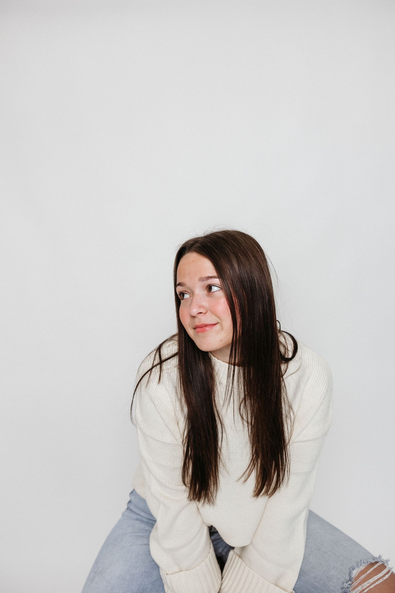 Young woman in cream sweater poses against white background in casual portrait series.