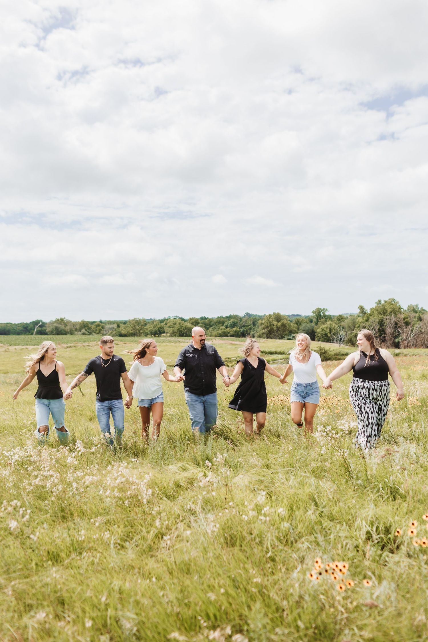 A family holding hands in a line across a sunny wildflower field.