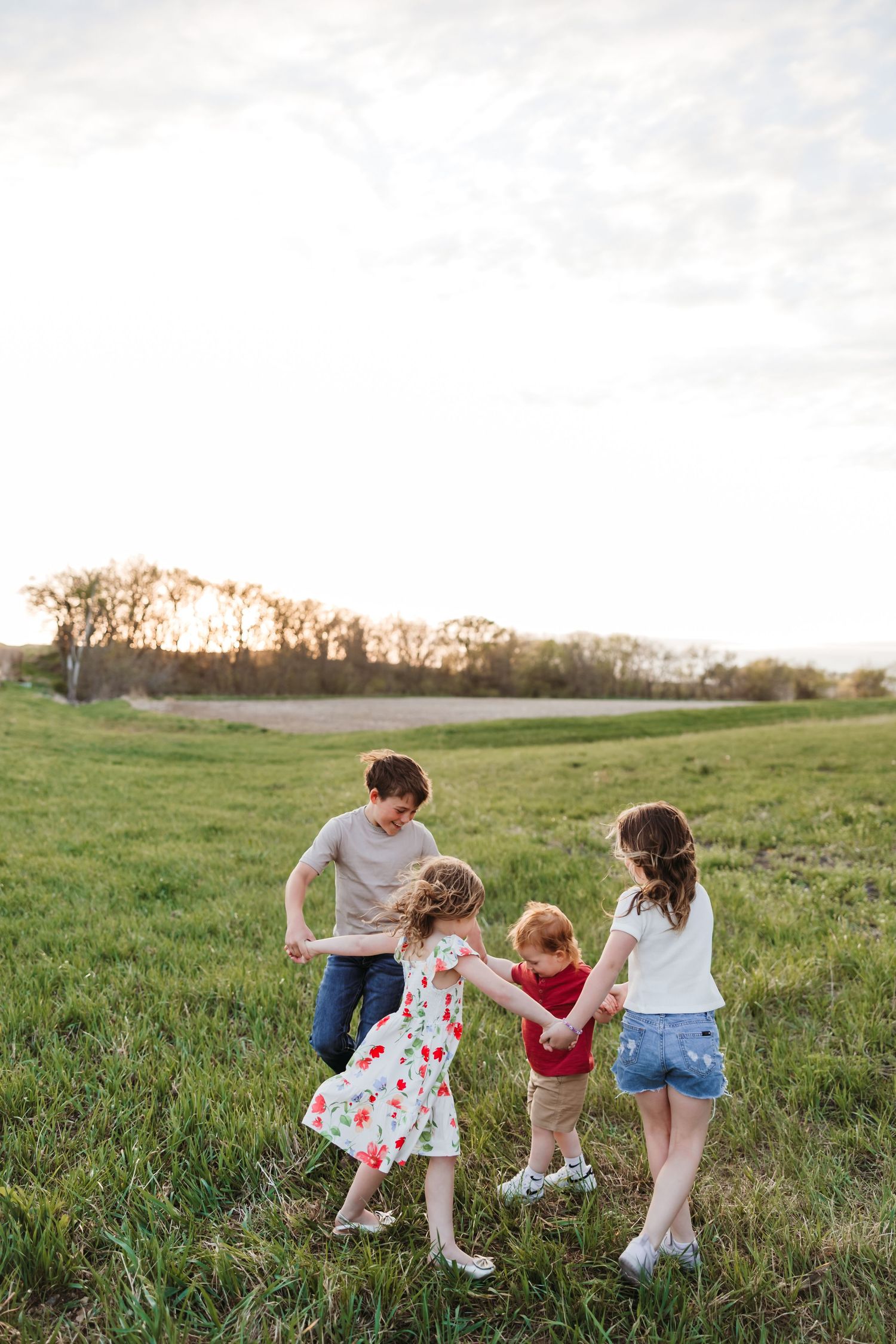 Four children holding hands and playing together in a green field at sunset.