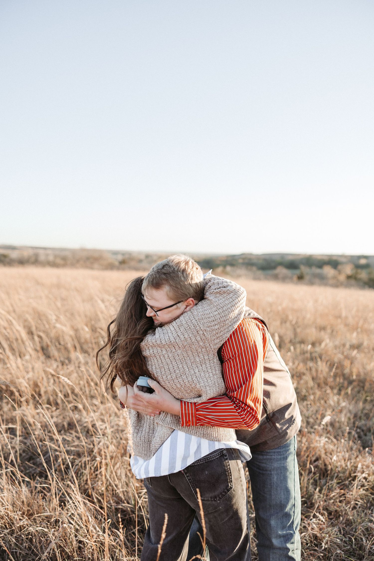 A couple embraces warmly in a sunlit field of tall grass.