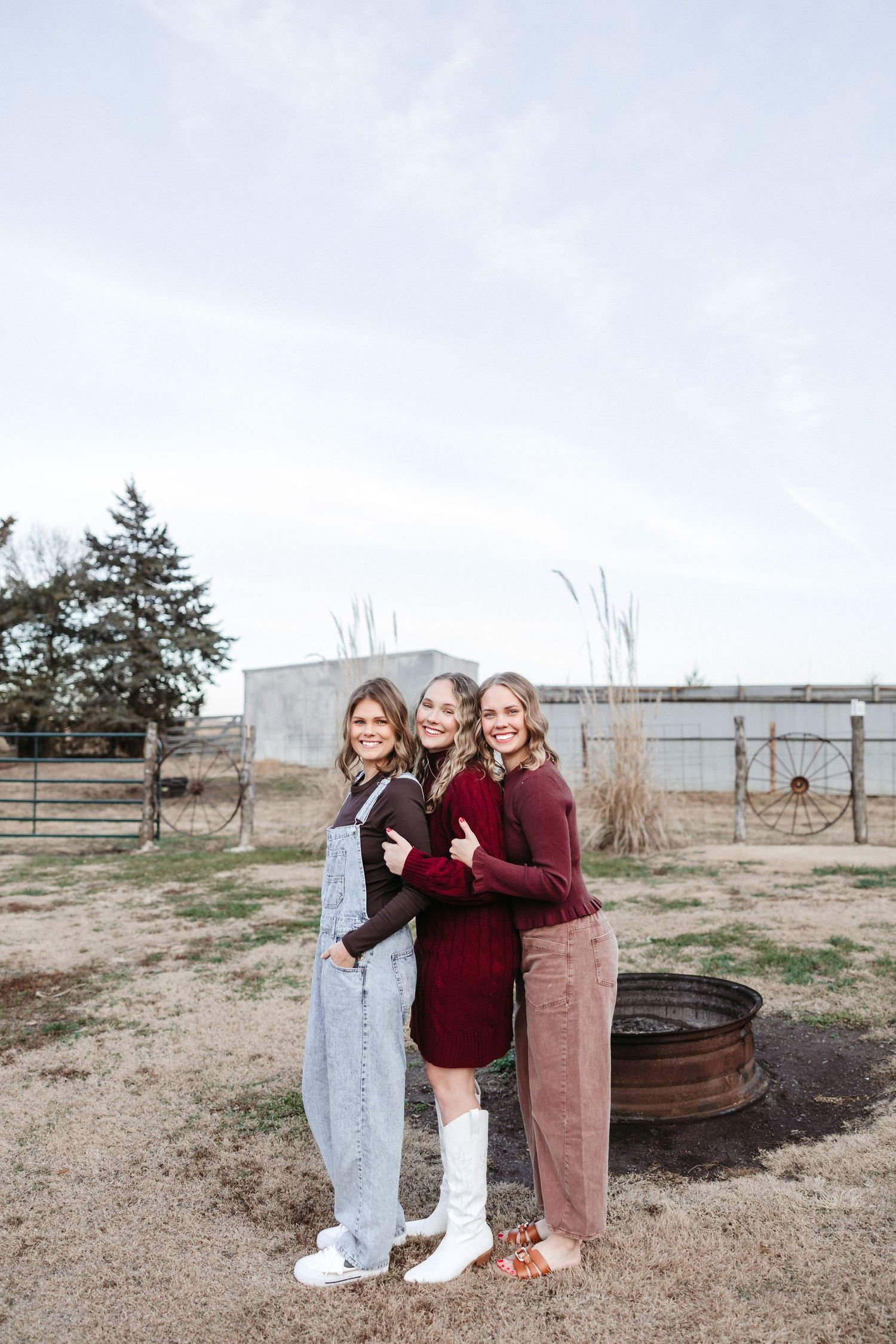 Three sisters posed together in casual clothing against a rural landscape backdrop.