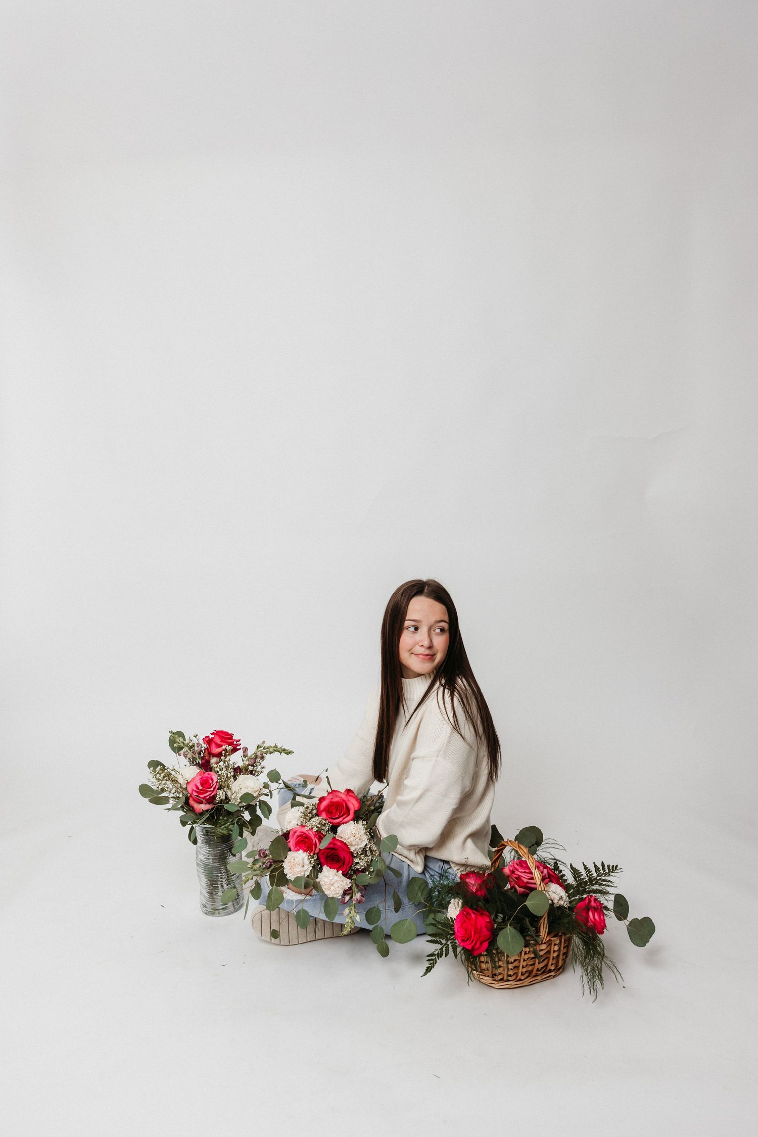 Playful pose with multiple floral arrangements against minimalist white backdrop.