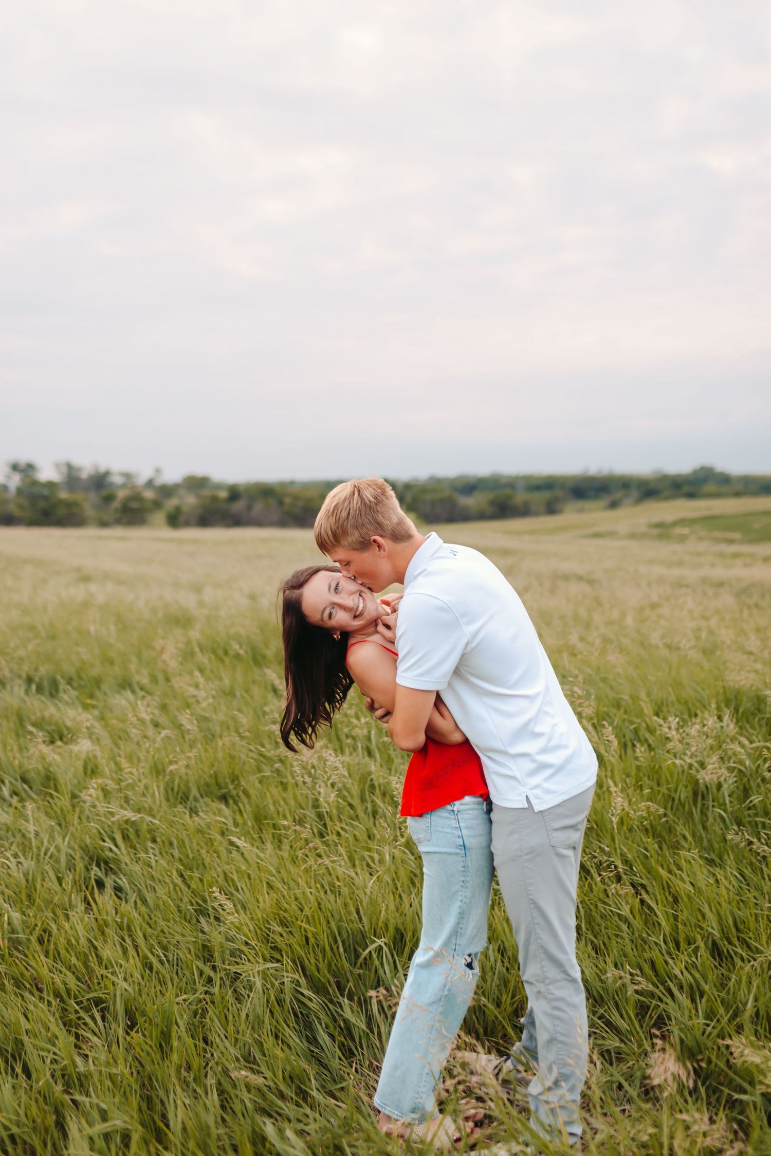 Playful couple dancing and laughing together in a tall grass meadow.