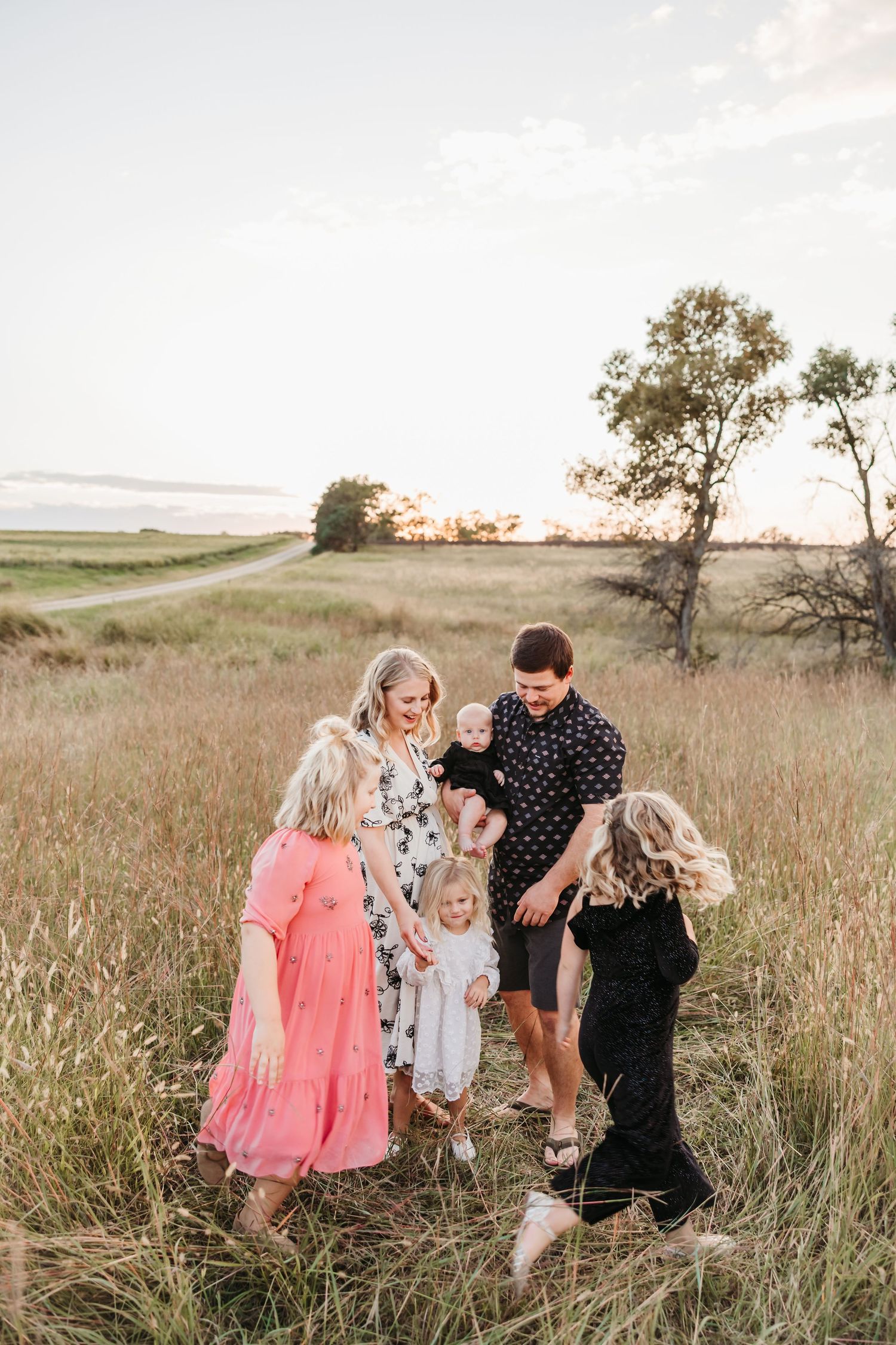 Playful family moment captured in a field with kids in pink and floral dresses.