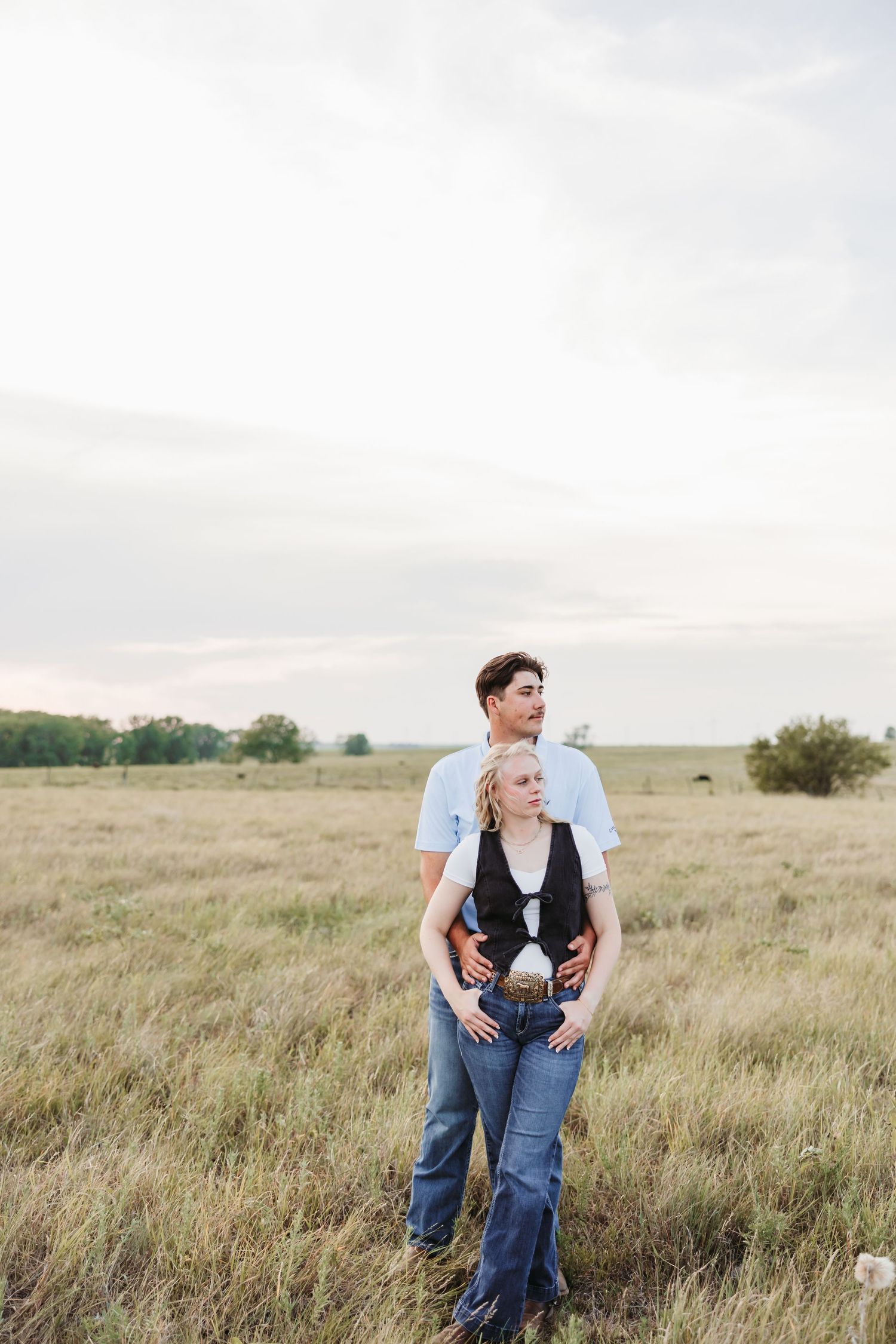 A couple poses together in a golden prairie field at sunset.