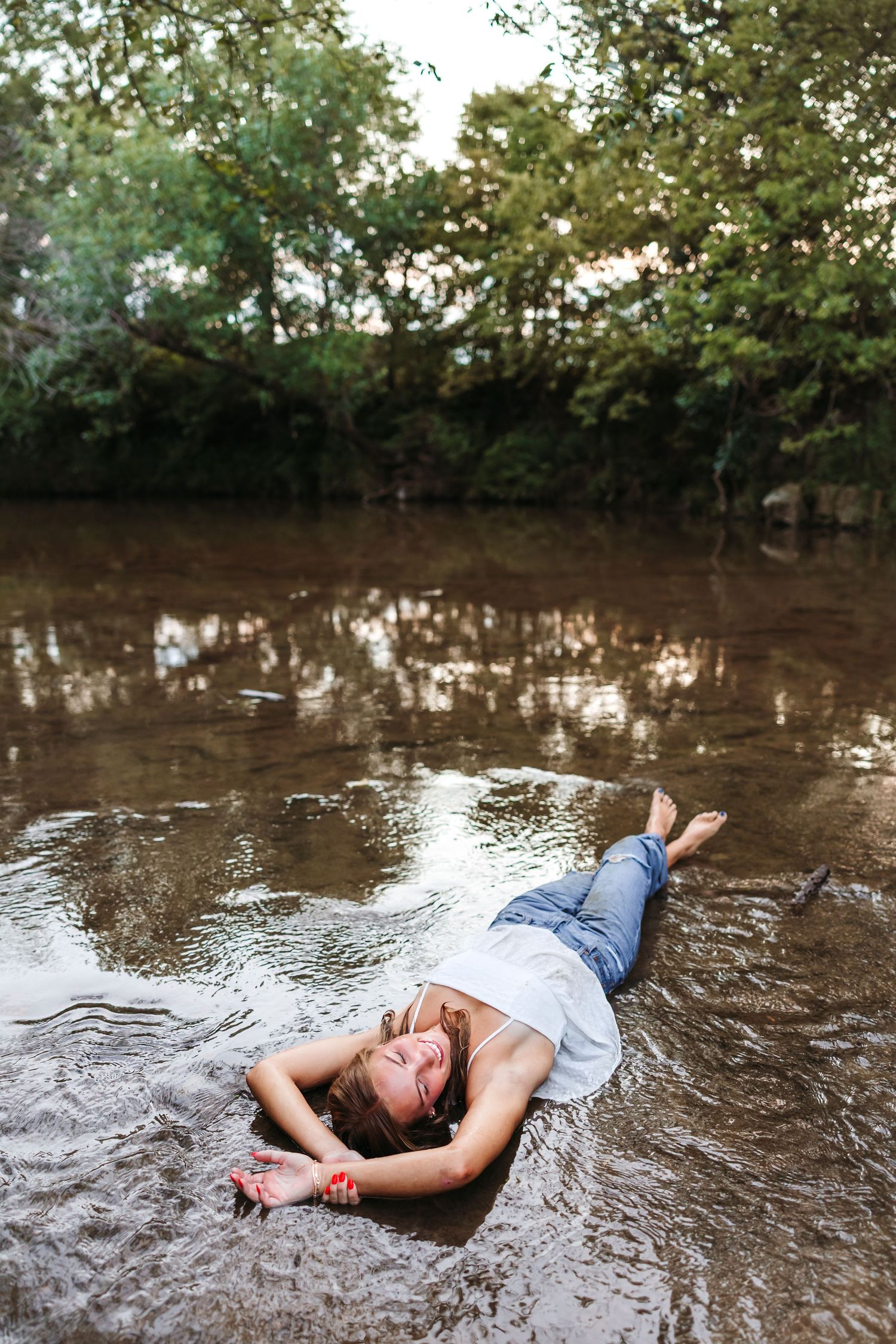 Artistic water portrait with person lying in shallow stream at sunset.