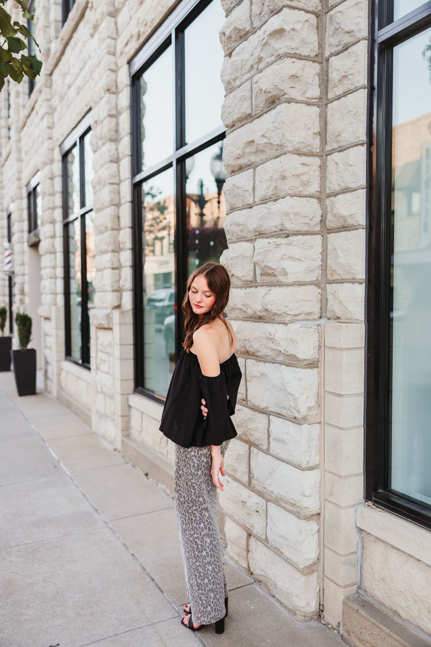 Portrait against stone wall featuring leopard print pants and black top.