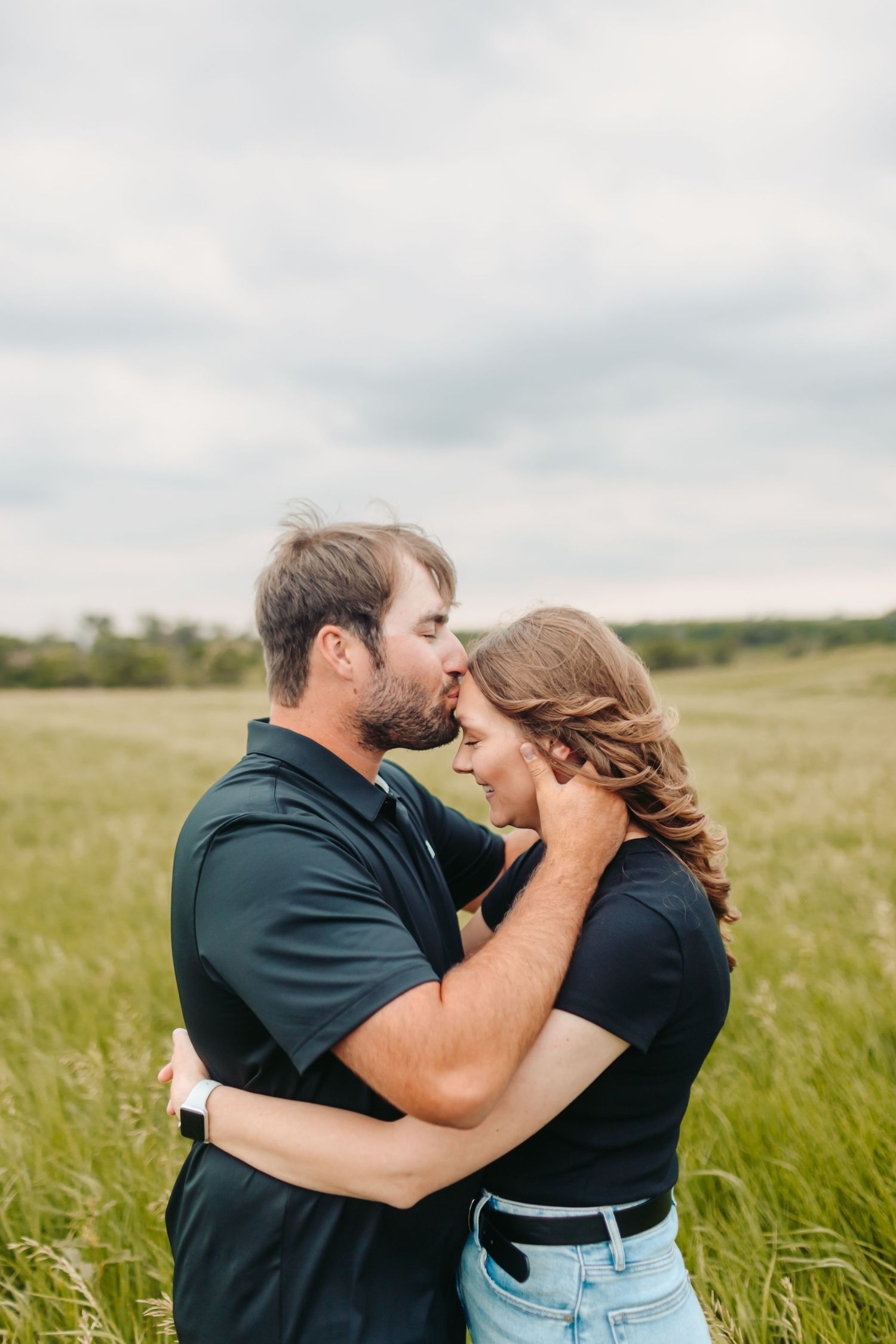 Couple embracing and laughing together in a green meadow under cloudy skies.