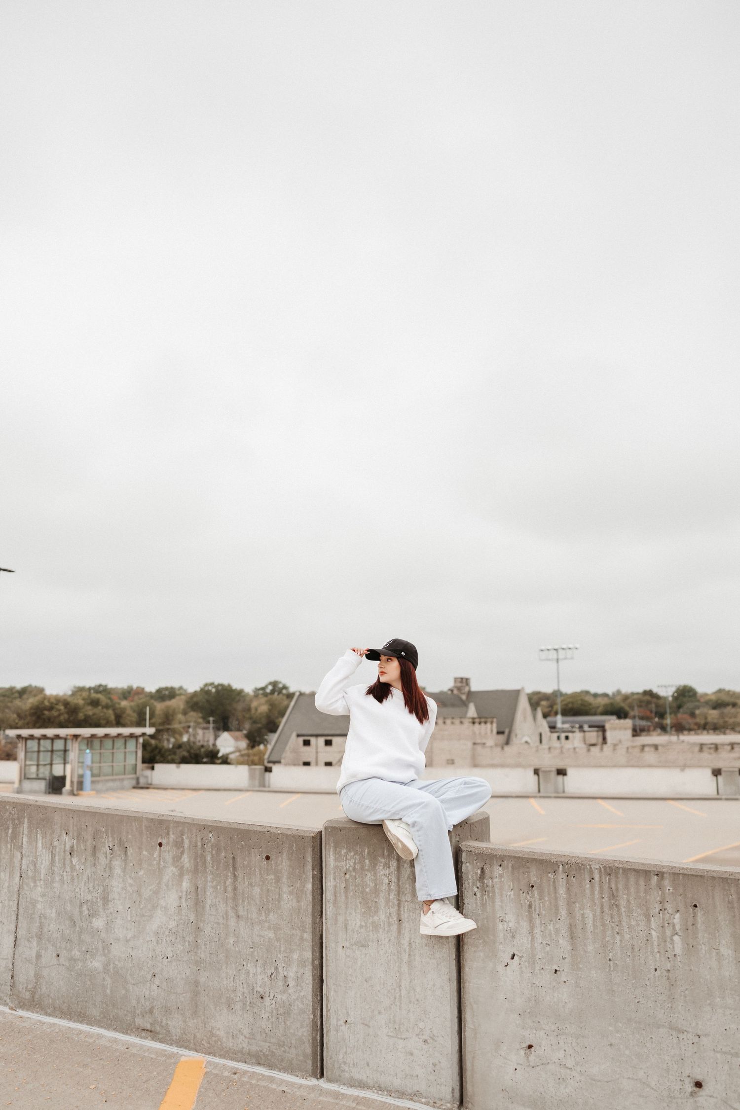 Person in white shirt sits on concrete barrier against cloudy sky.