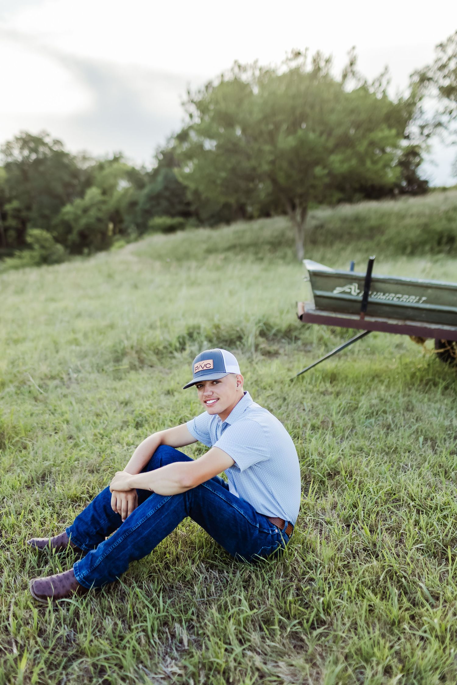 Casual outdoor portrait on grassy hillside with boat in background.