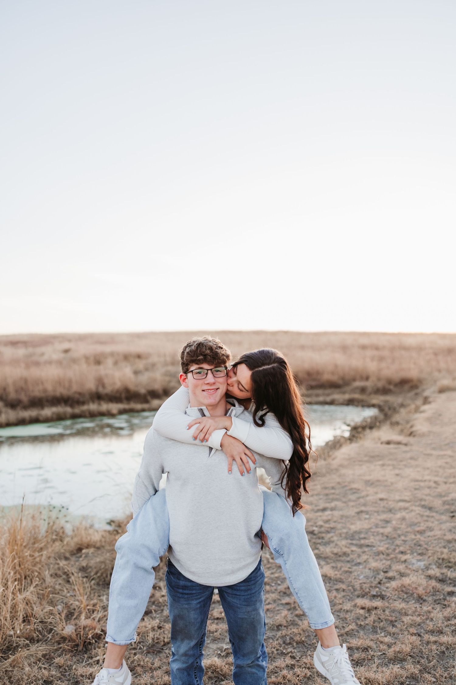 A playful piggyback ride moment between a couple on a scenic trail near a pond.