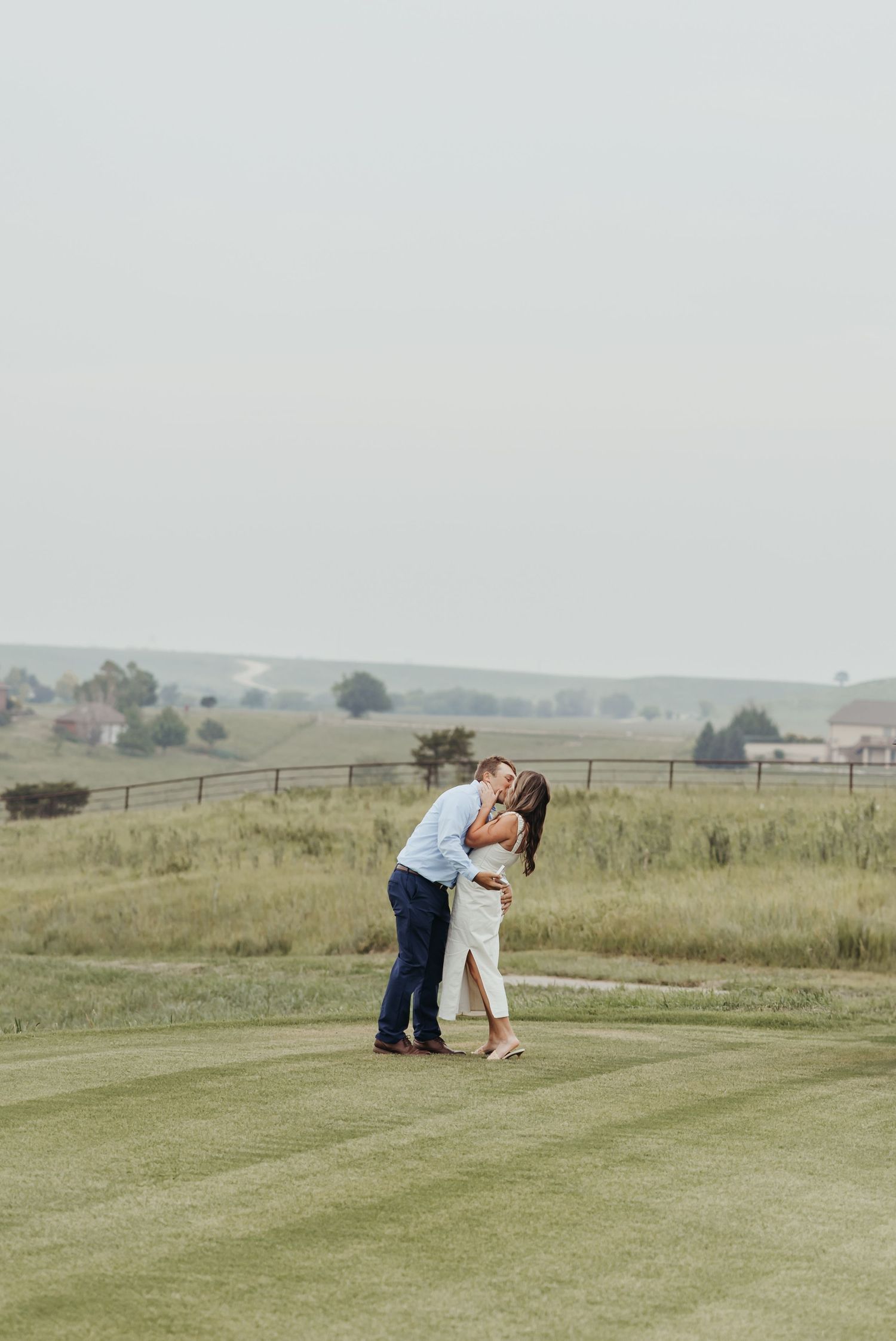A couple shares a romantic moment on a manicured golf course with countryside views.