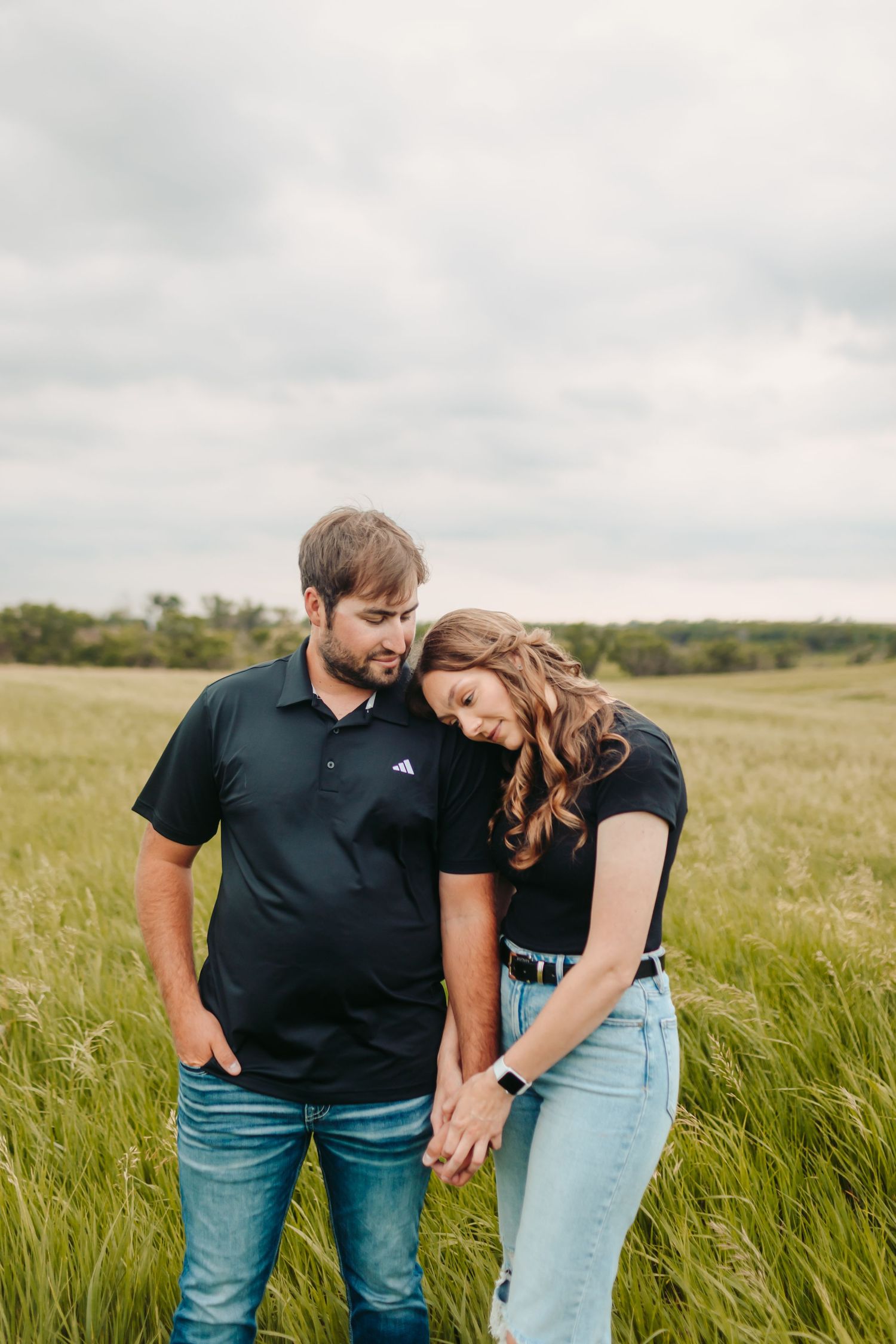 Couple leaning together affectionately in a rustic field setting.