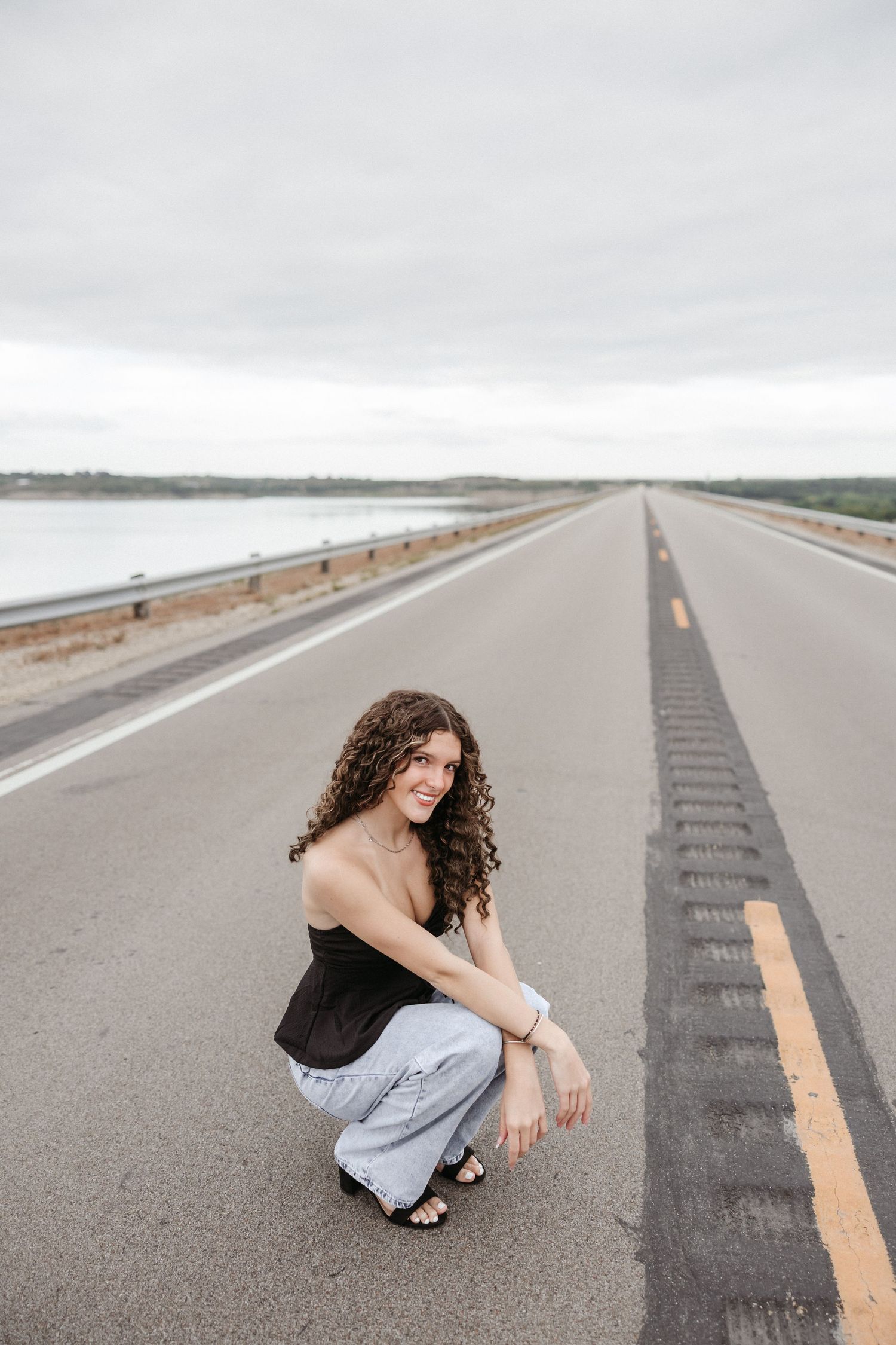 Person posing on empty highway with dramatic cloudy sky.